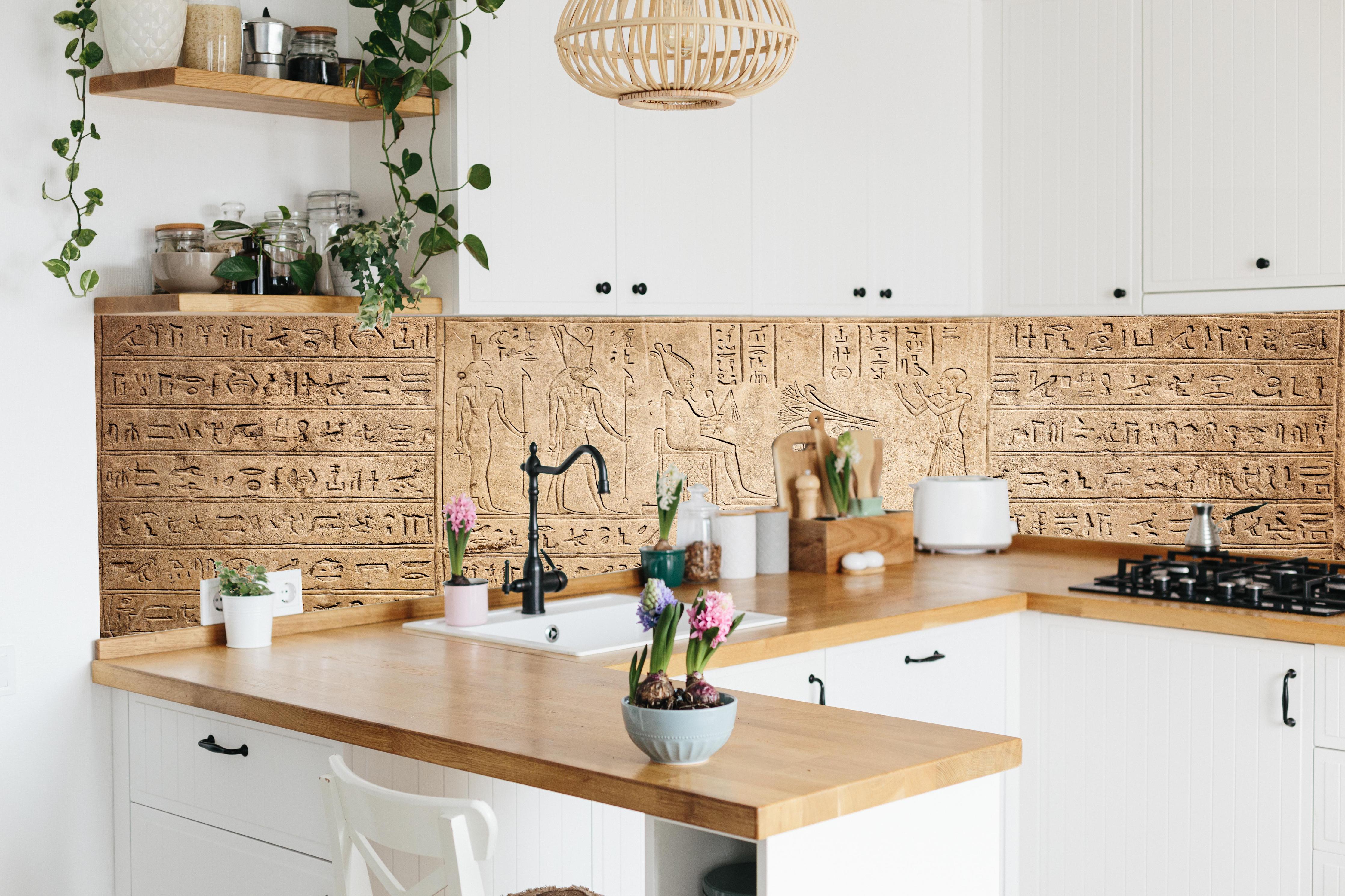 Küche - Ägyptische Hieroglyphen auf Sandstein hinter weißen Hochglanz-Küchenregalen und schwarzem Wasserhahn