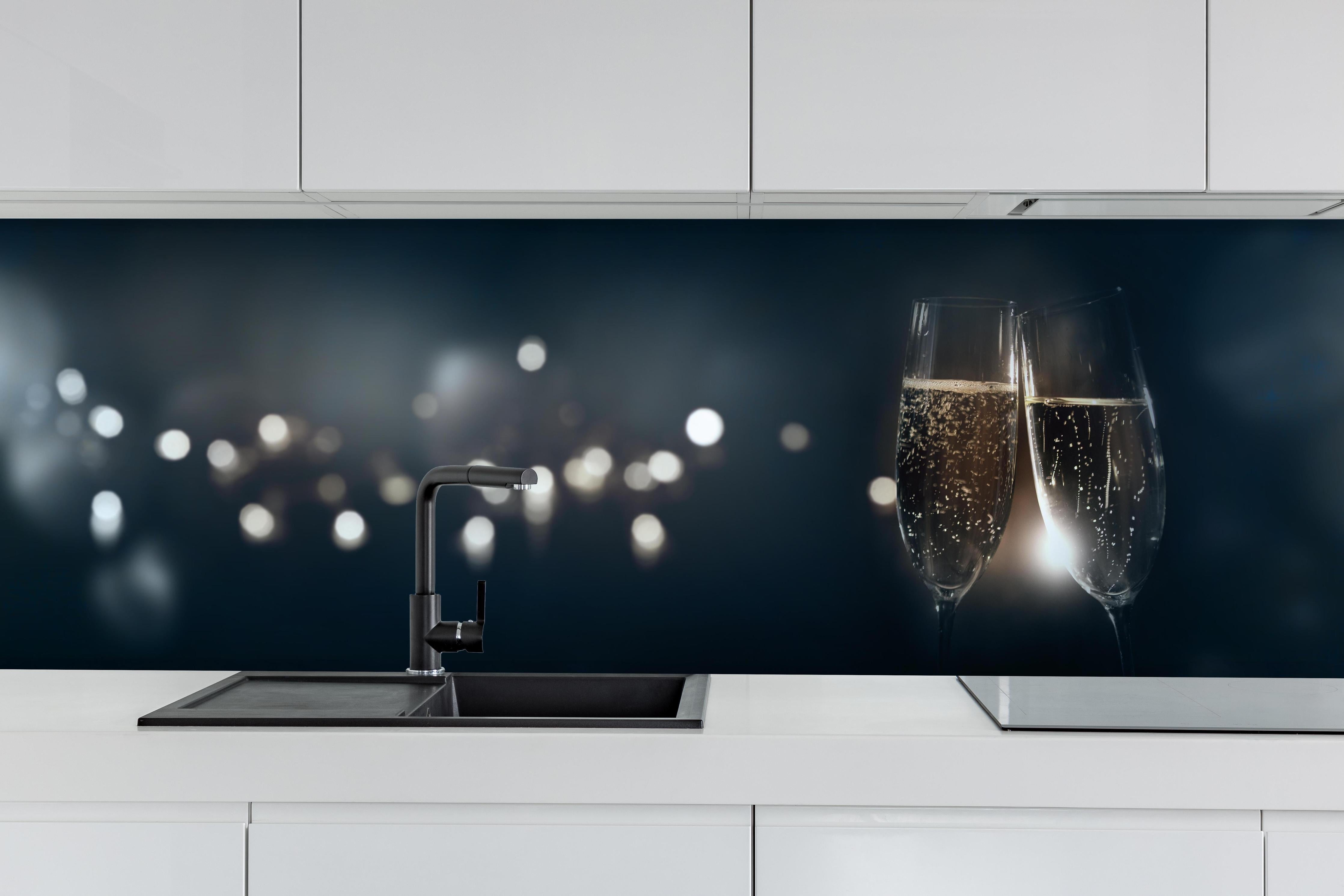 Küche - Anstoßen mit funkelndem Champagner hinter weißen Hochglanz-Küchenregalen und schwarzem Wasserhahn