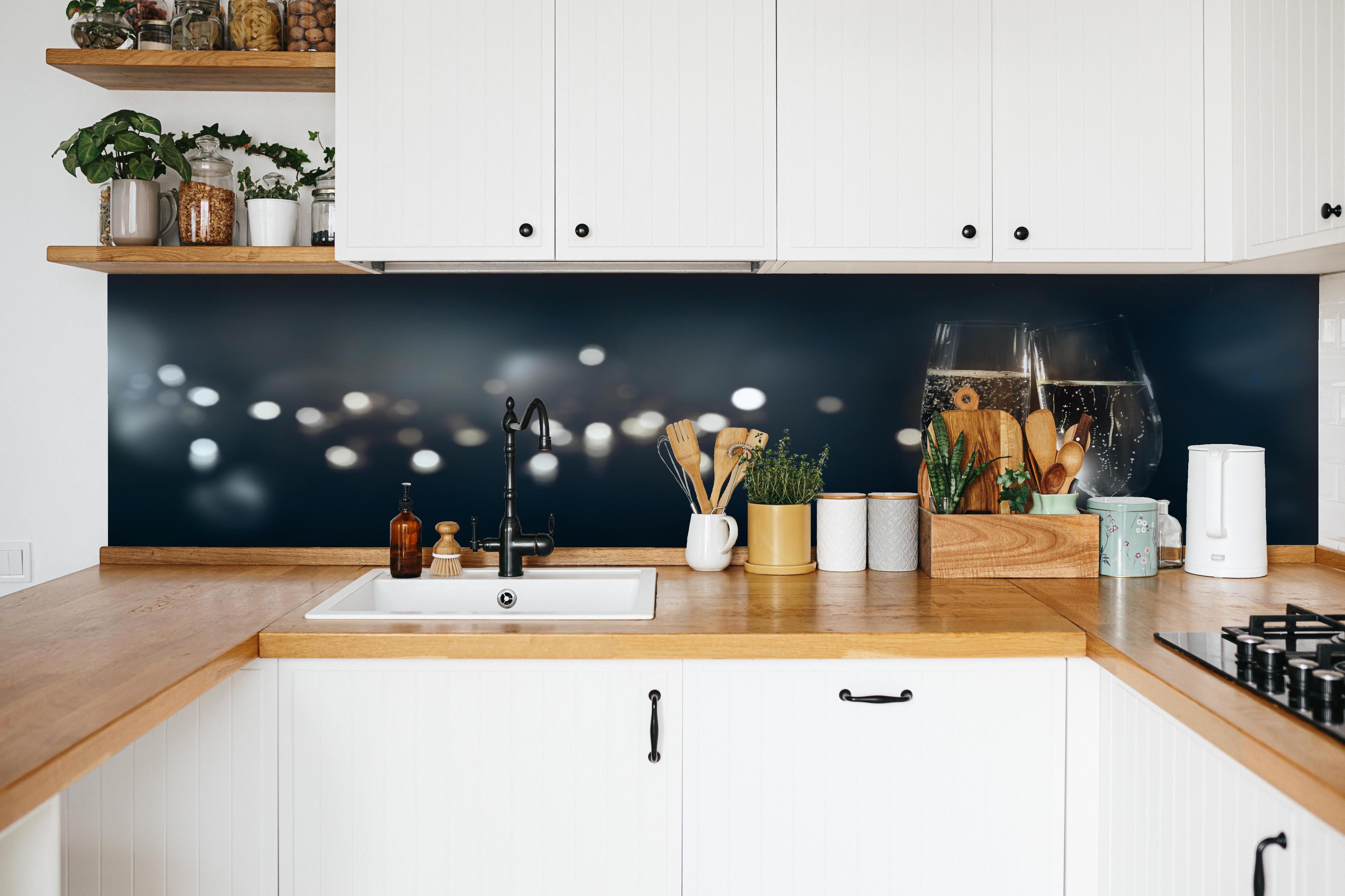 Küche - Anstoßen mit funkelndem Champagner hinter weißen Hochglanz-Küchenregalen und schwarzem Wasserhahn