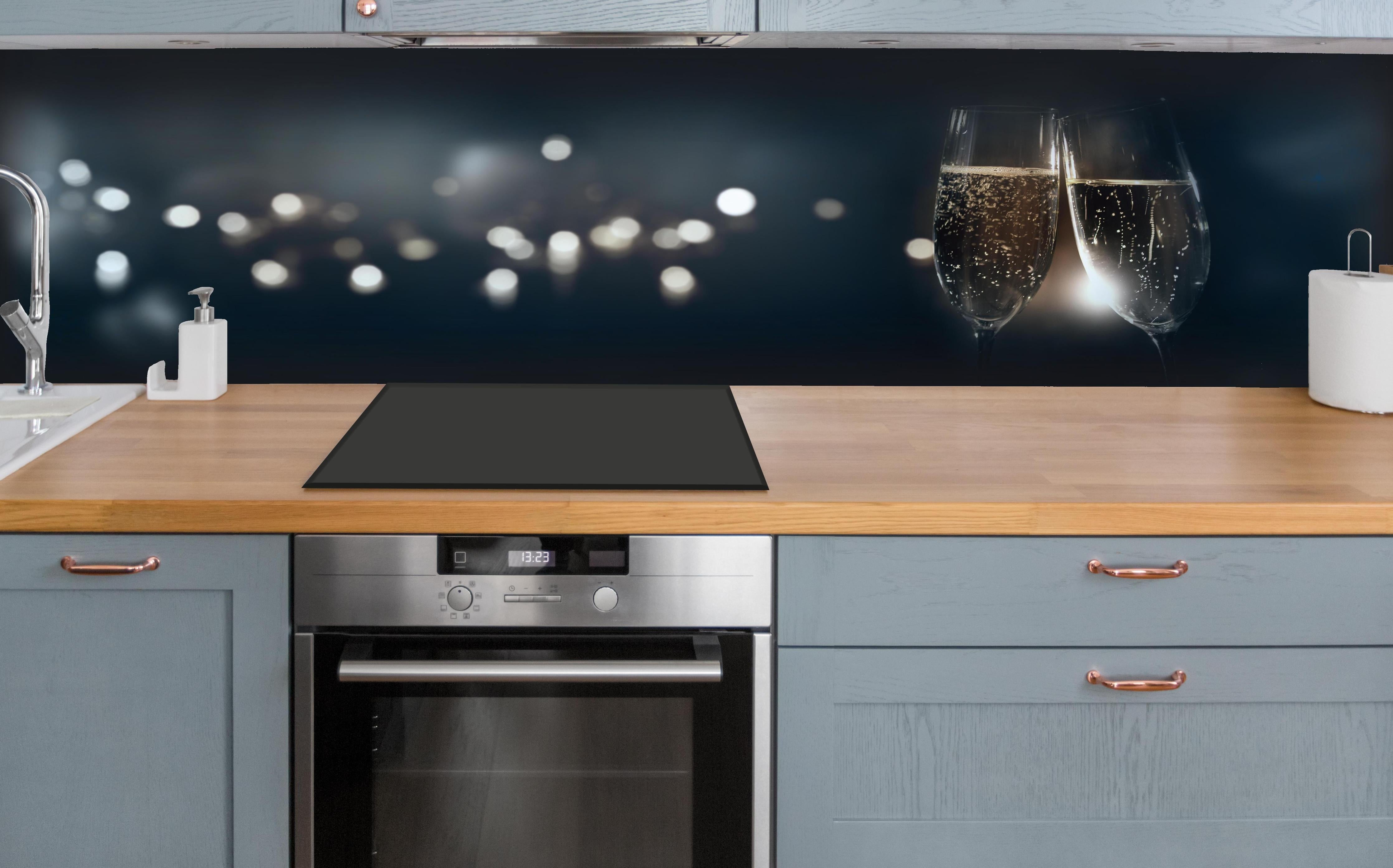 Küche - Anstoßen mit funkelndem Champagner hinter weißen Hochglanz-Küchenregalen und schwarzem Wasserhahn