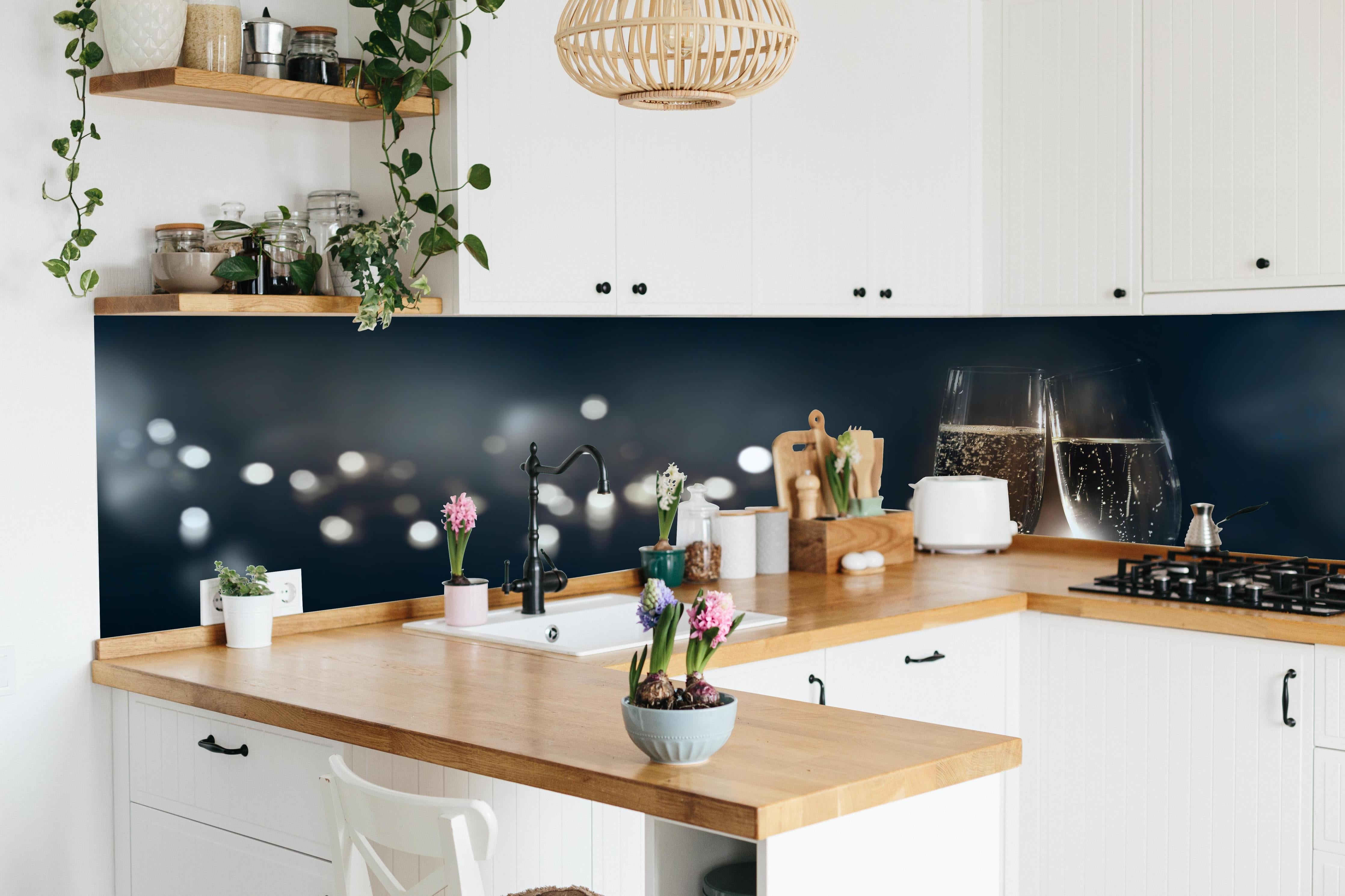 Küche - Anstoßen mit funkelndem Champagner hinter weißen Hochglanz-Küchenregalen und schwarzem Wasserhahn