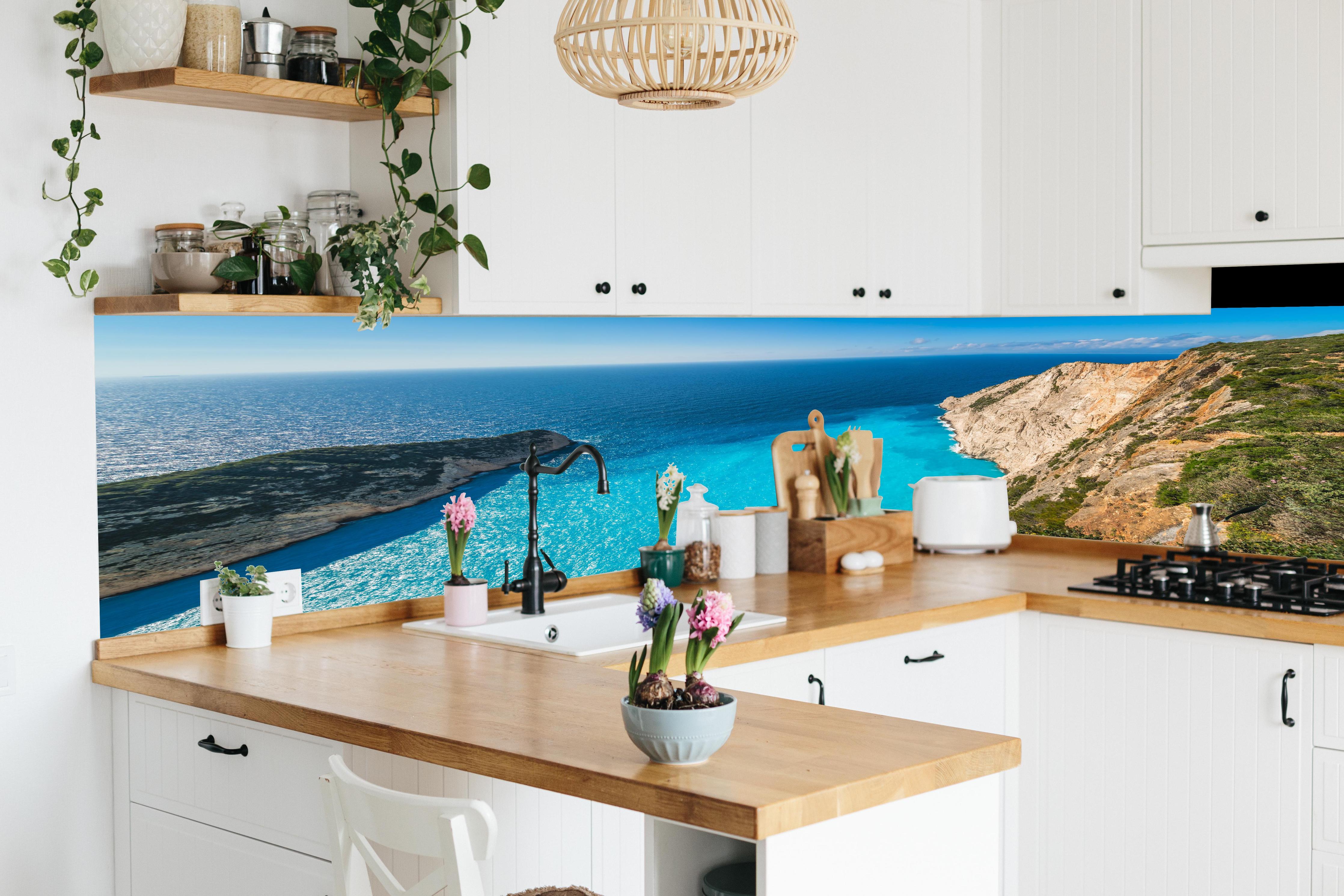 Küche - Atemberaubende Aussicht auf türkisblaue Küstenlandschaft hinter weißen Hochglanz-Küchenregalen und schwarzem Wasserhahn