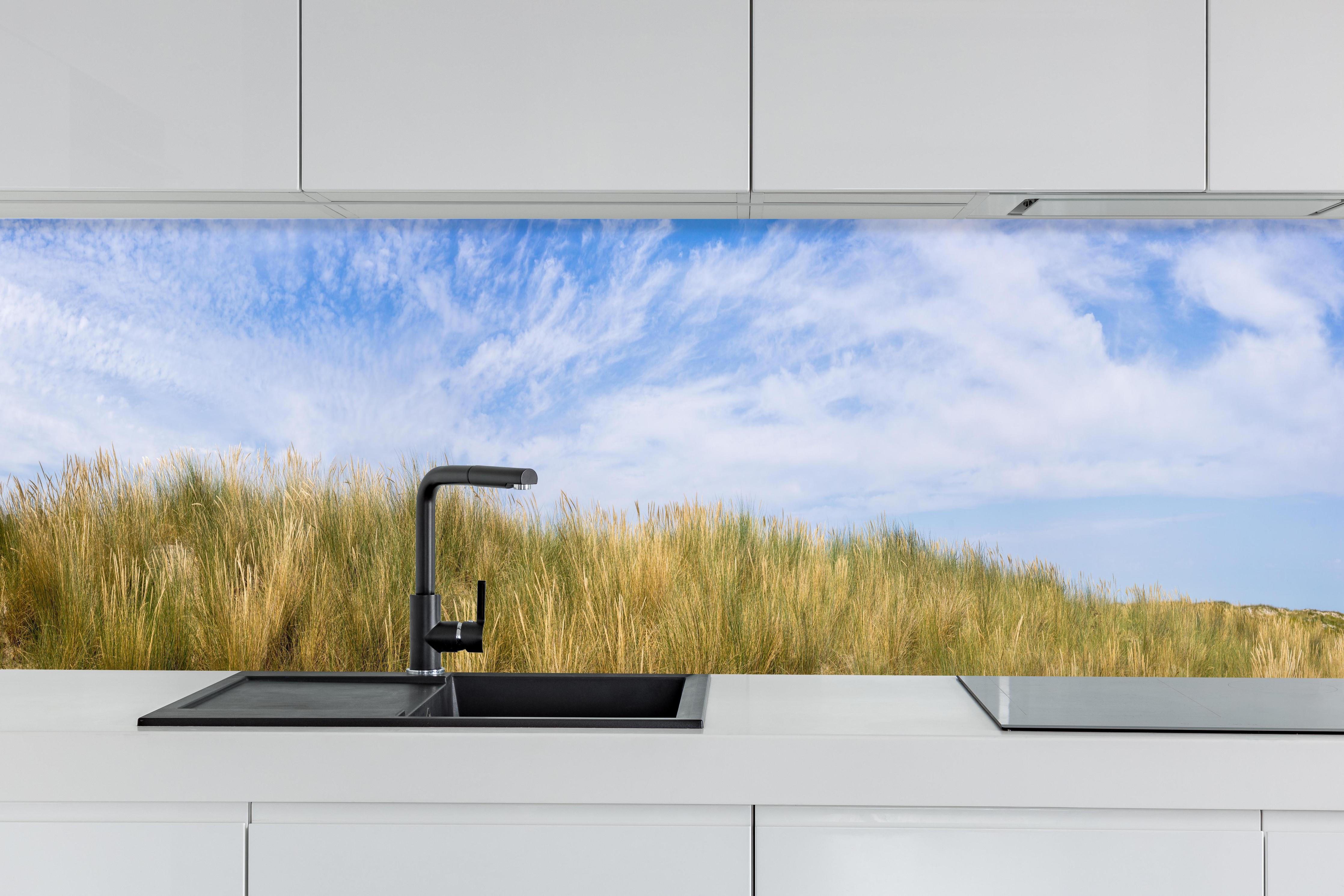 Küche - Atemberaubende Küstenlandschaft unter blauem Himmel hinter weißen Hochglanz-Küchenregalen und schwarzem Wasserhahn