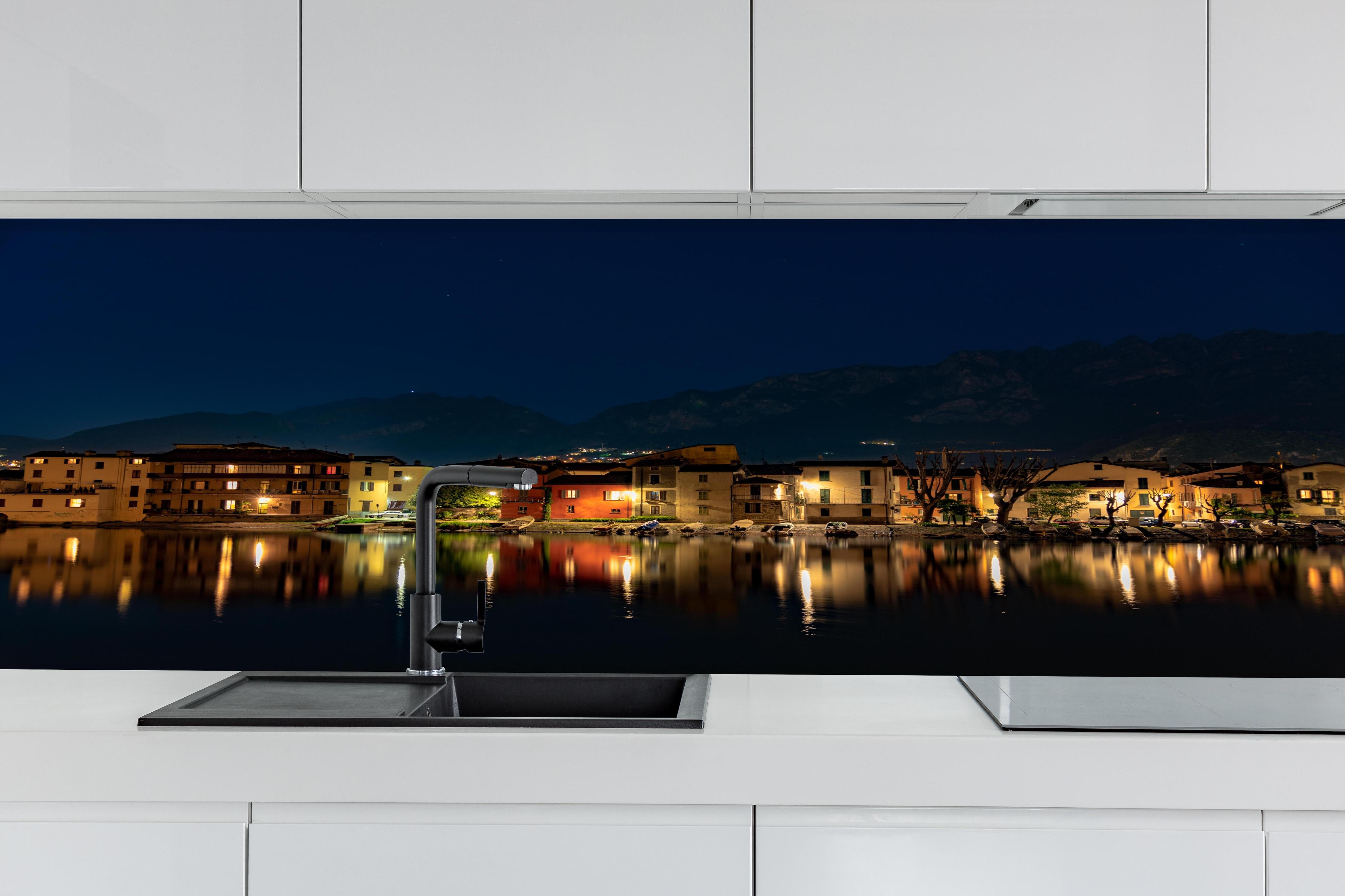 Küche - Beleuchtete Seelandschaft bei Nacht hinter weißen Hochglanz-Küchenregalen und schwarzem Wasserhahn