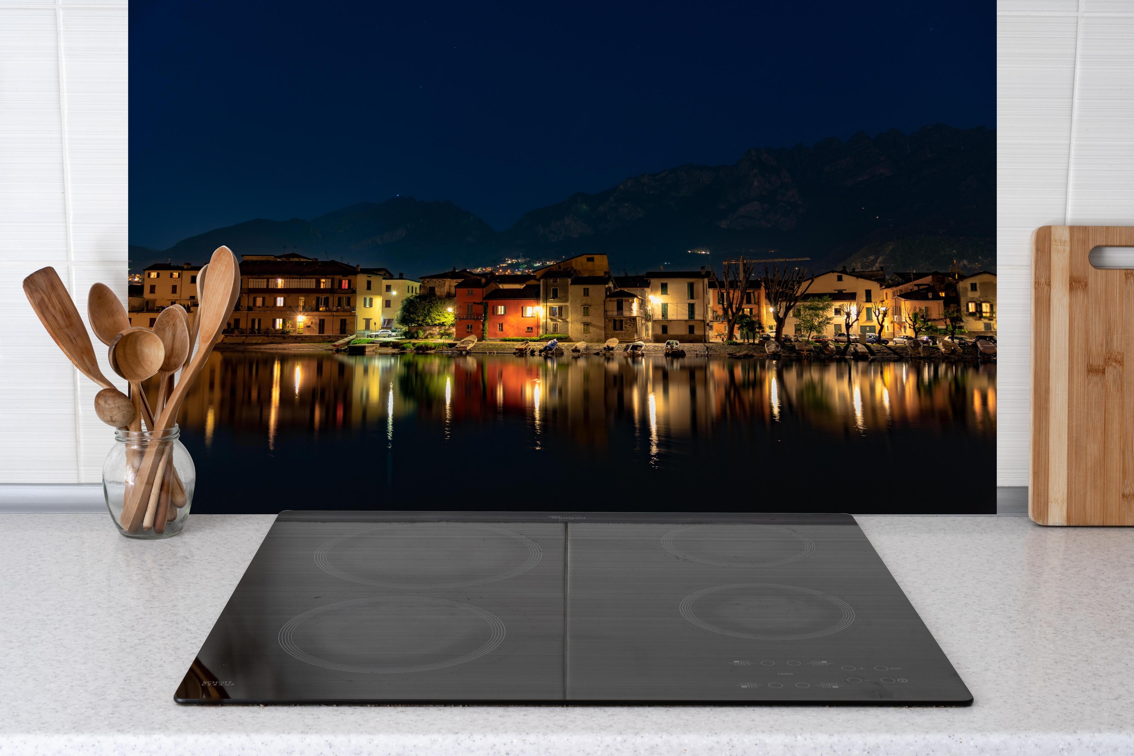 Küche - Beleuchtete Seelandschaft bei Nacht hinter weißen Hochglanz-Küchenregalen und schwarzem Wasserhahn