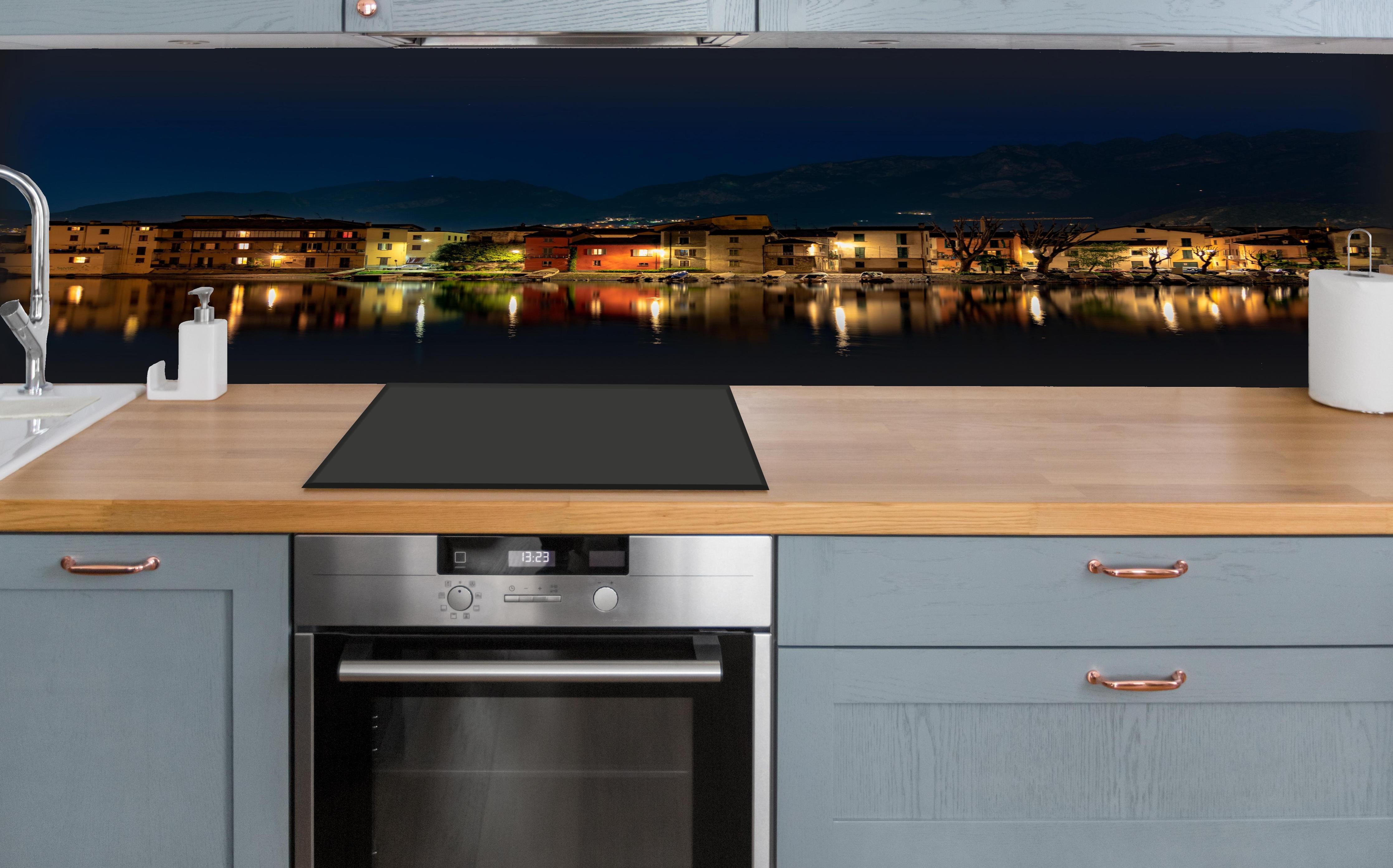 Küche - Beleuchtete Seelandschaft bei Nacht hinter weißen Hochglanz-Küchenregalen und schwarzem Wasserhahn