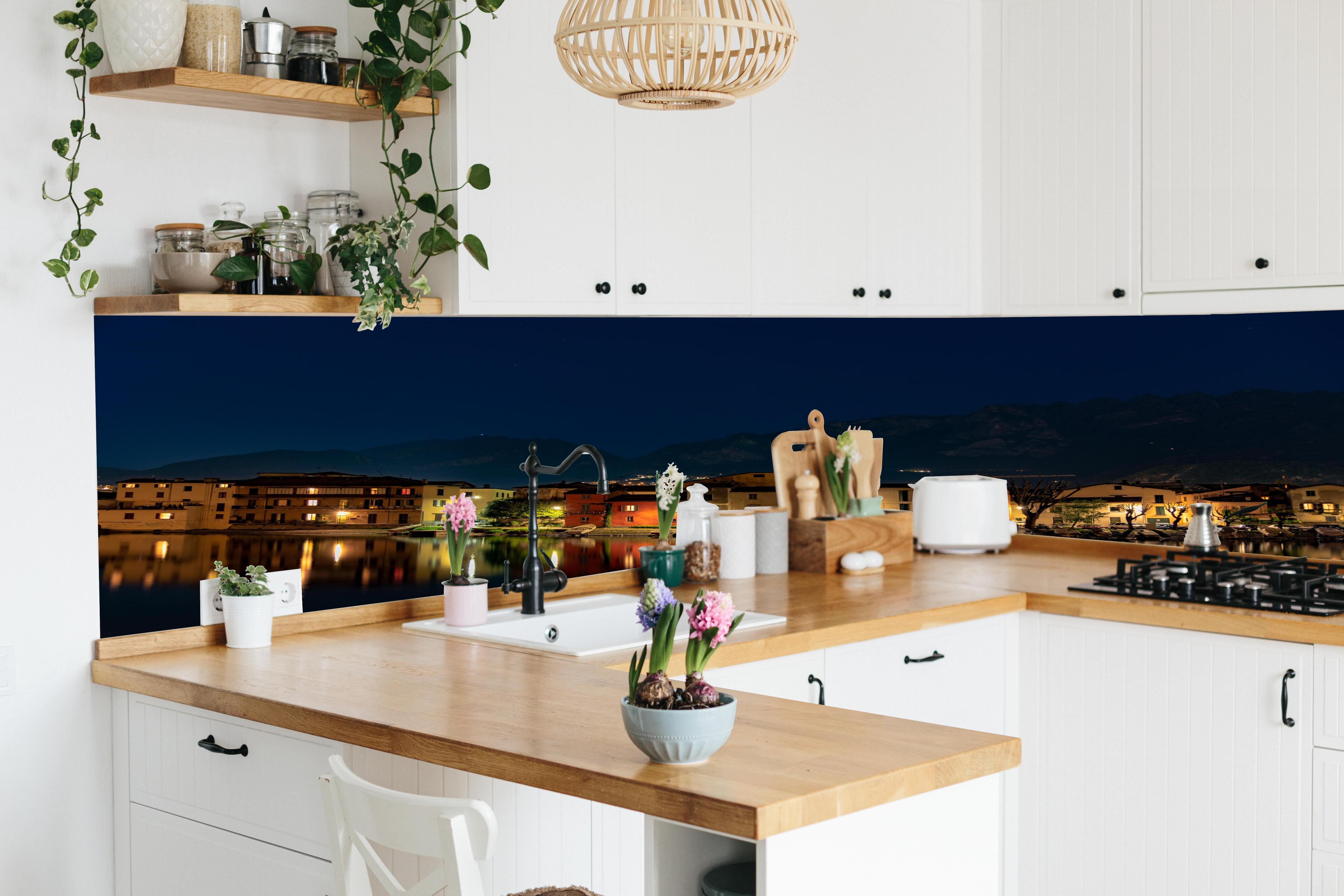 Küche - Beleuchtete Seelandschaft bei Nacht hinter weißen Hochglanz-Küchenregalen und schwarzem Wasserhahn