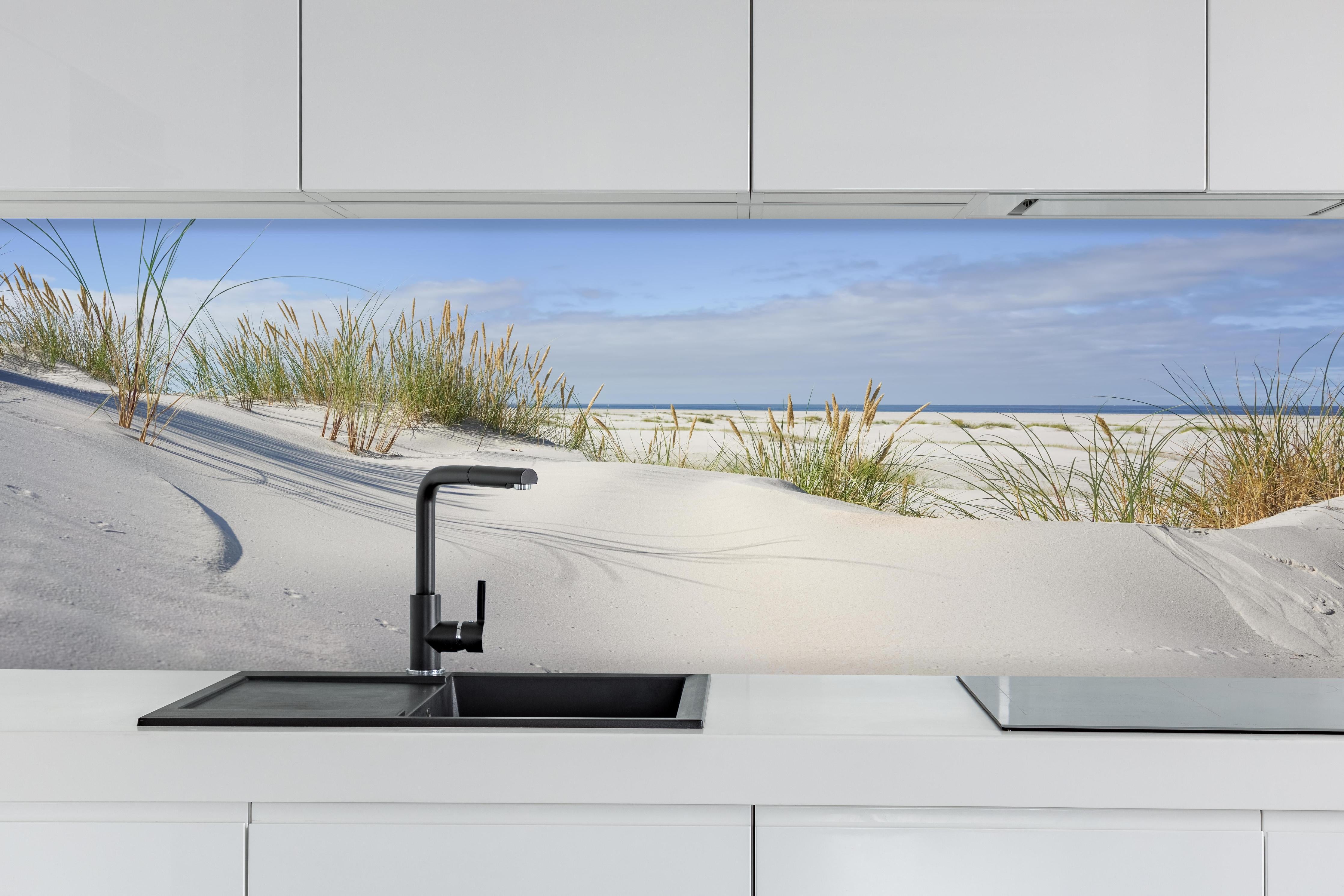 Küche - Beruhigende weiße Dünenlandschaft mit sanften Gräsern am Ozean hinter weißen Hochglanz-Küchenregalen und schwarzem Wasserhahn