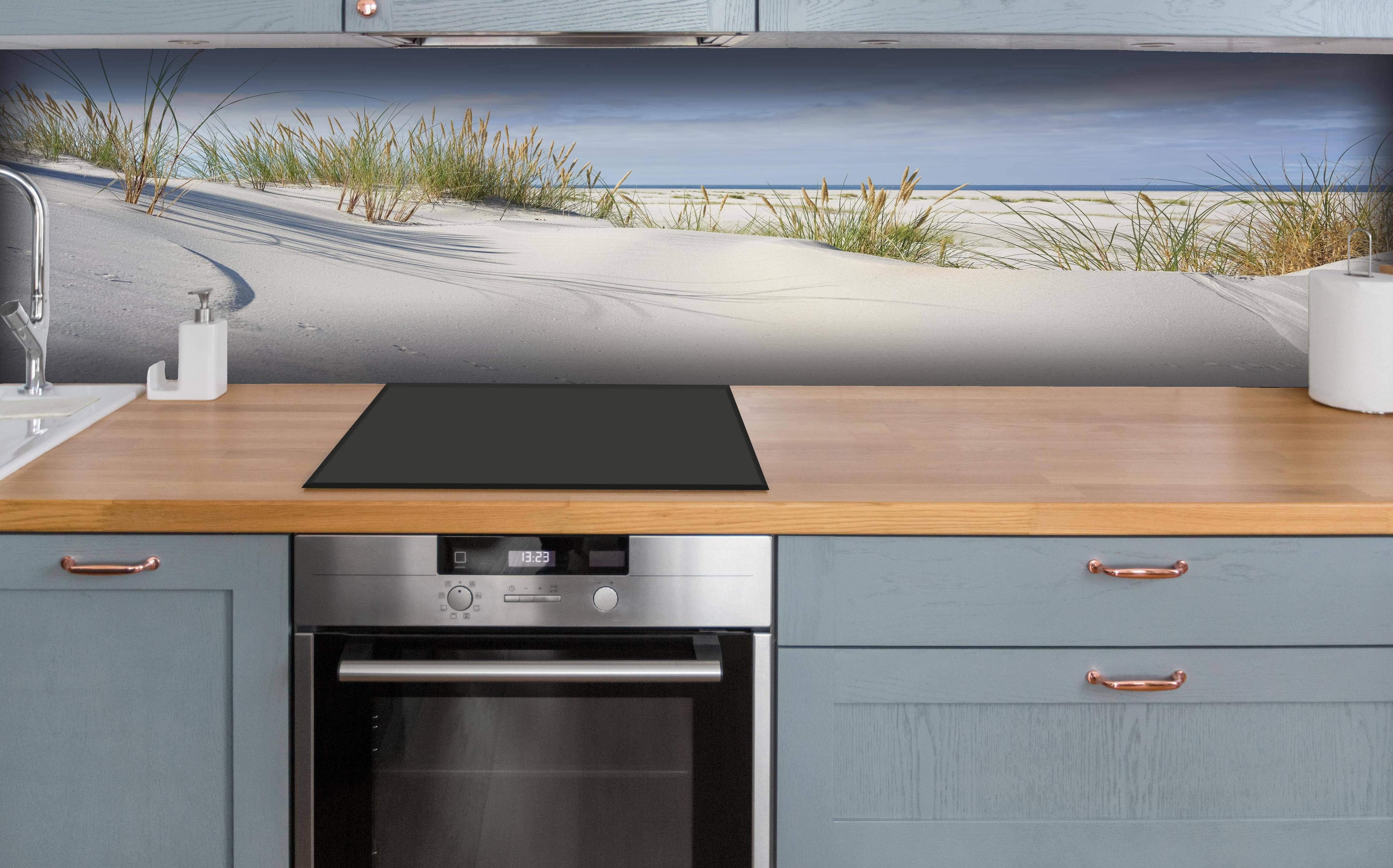 Küche - Beruhigende weiße Dünenlandschaft mit sanften Gräsern am Ozean hinter weißen Hochglanz-Küchenregalen und schwarzem Wasserhahn