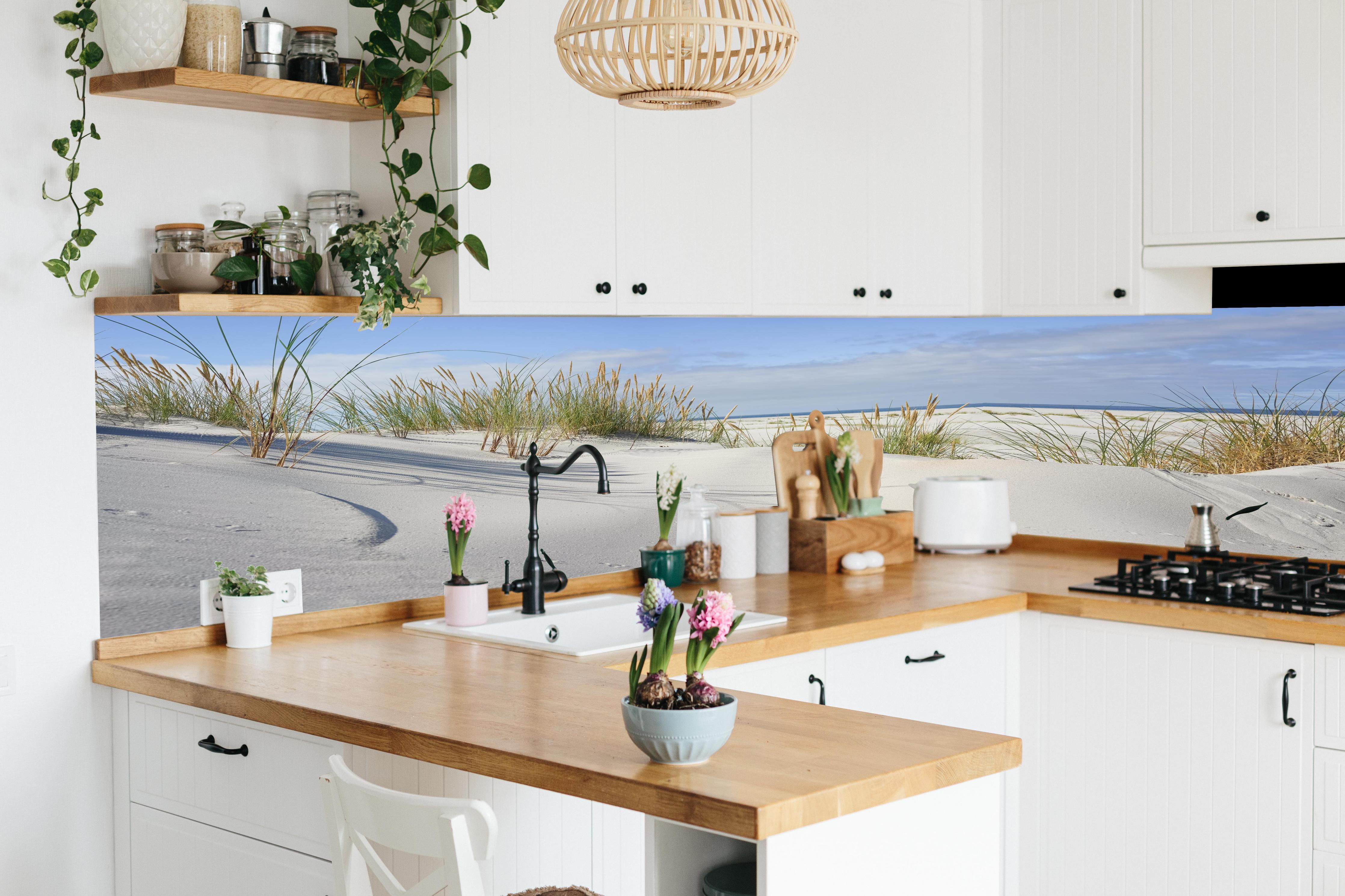 Küche - Beruhigende weiße Dünenlandschaft mit sanften Gräsern am Ozean hinter weißen Hochglanz-Küchenregalen und schwarzem Wasserhahn
