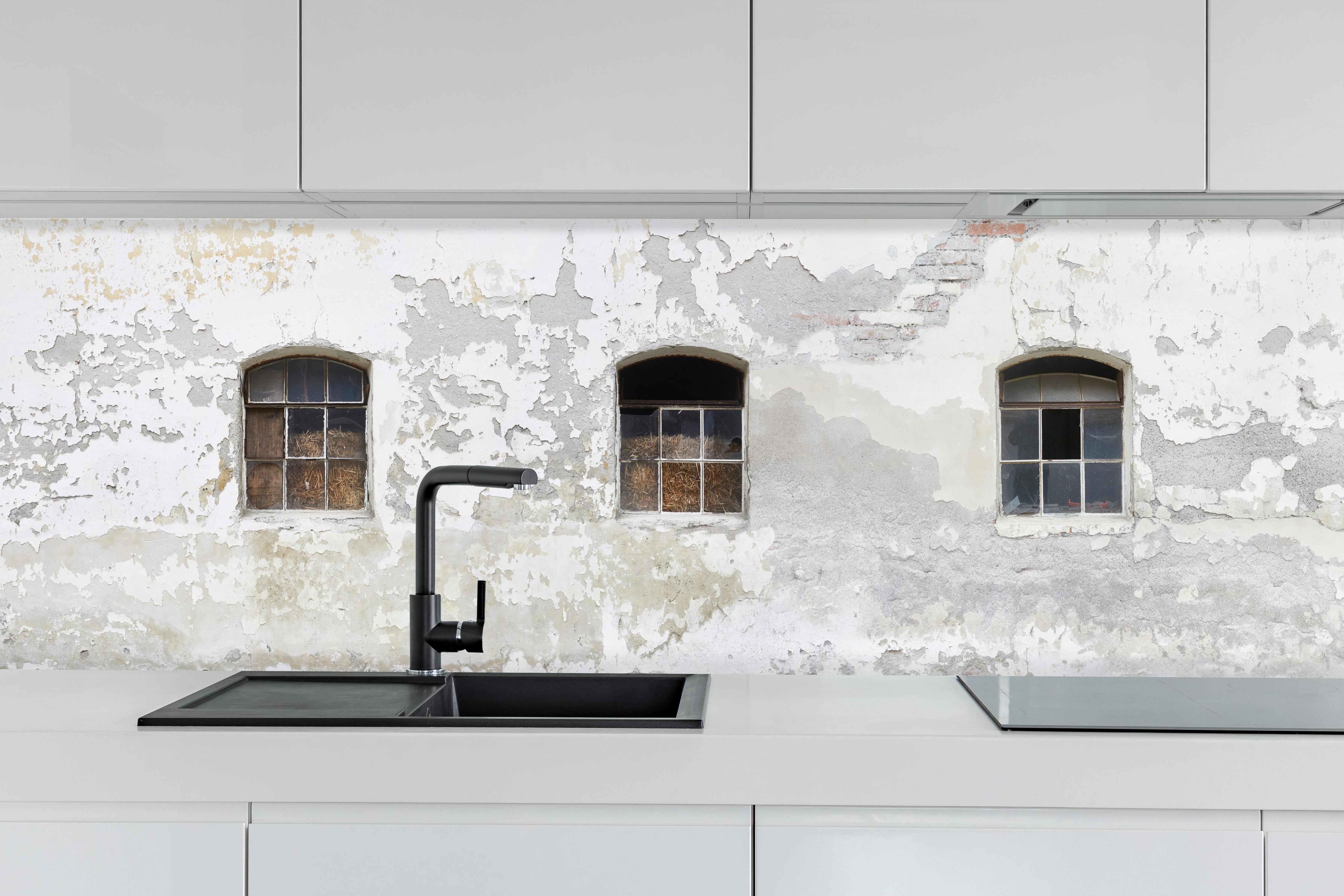 Küche - Beschädigte Fenster einer veralteten Hauswand hinter weißen Hochglanz-Küchenregalen und schwarzem Wasserhahn