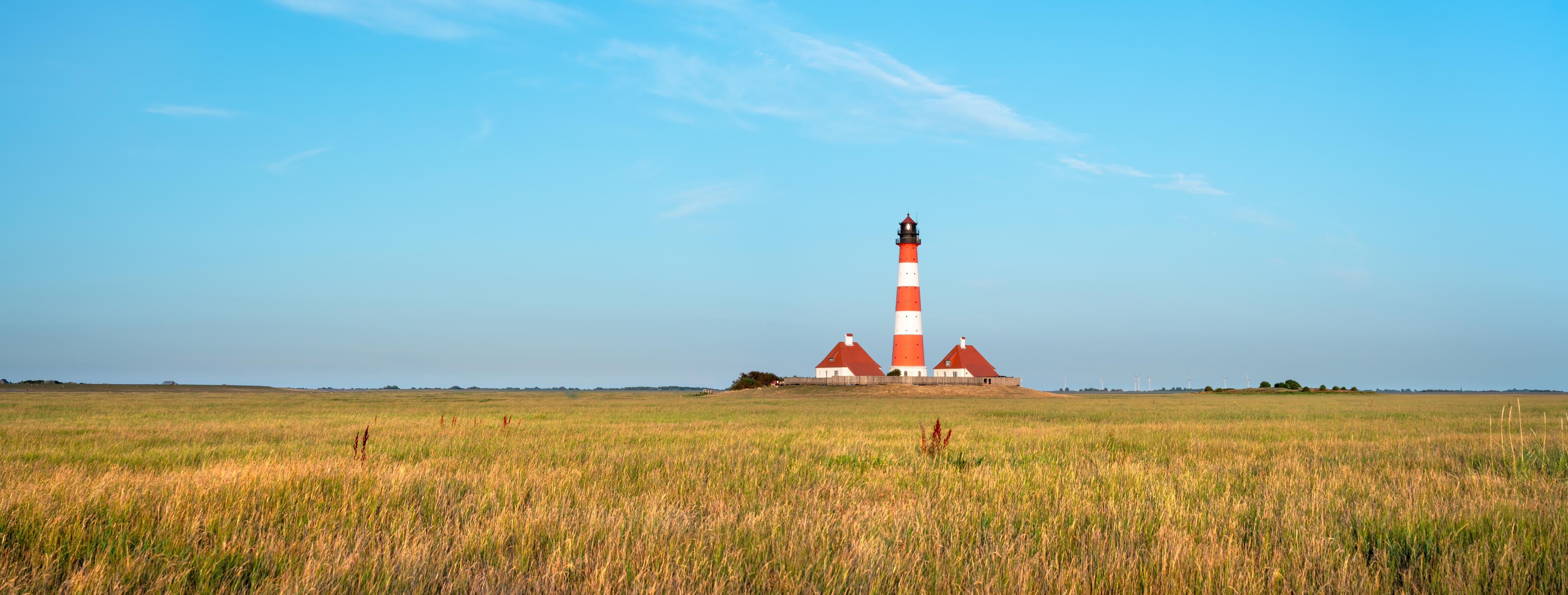 Küchenrückwand-Ein beeindruckender Leuchtturm in der weitläufigen norddeutschen Landschaft unter blauem Himmel.