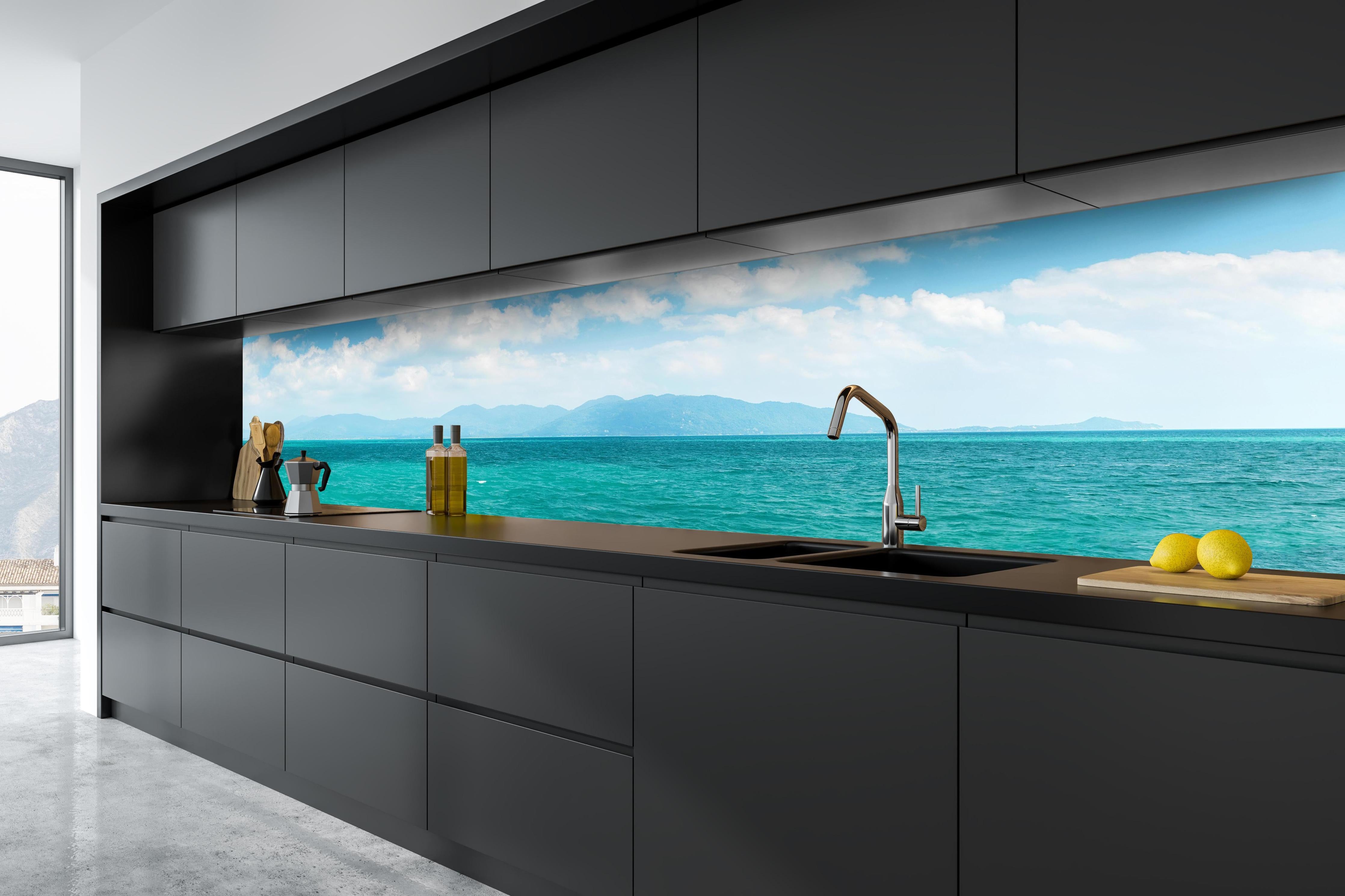 Küche - Ein beeindruckendes Panorama des Ozeans unter einem klaren blauen Himmel mit sanften Wellen und malerischen Bergen im Hintergrund. hinter weißen Hochglanz-Küchenregalen und schwarzem Wasserhahn