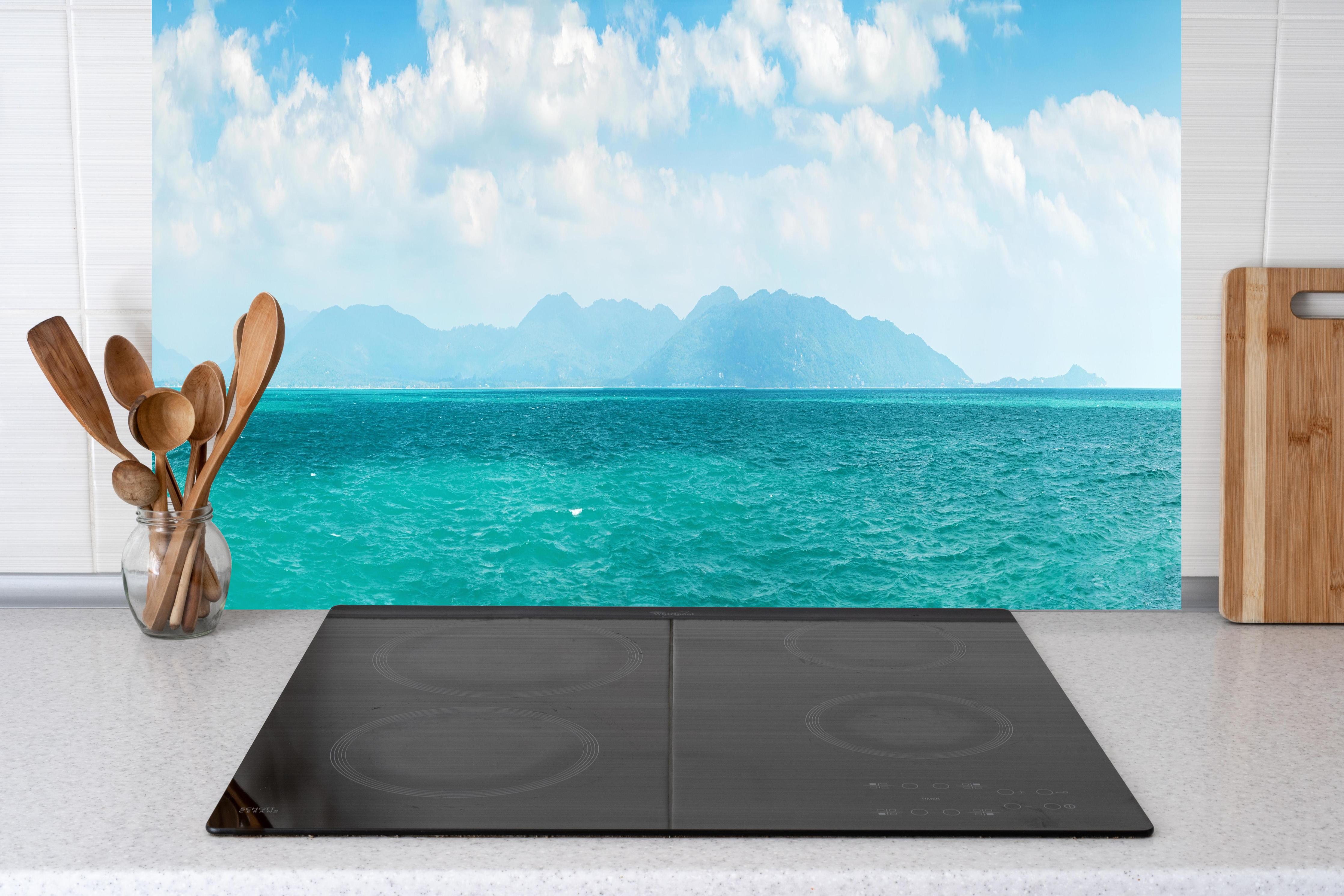 Küche - Ein beeindruckendes Panorama des Ozeans unter einem klaren blauen Himmel mit sanften Wellen und malerischen Bergen im Hintergrund. hinter weißen Hochglanz-Küchenregalen und schwarzem Wasserhahn