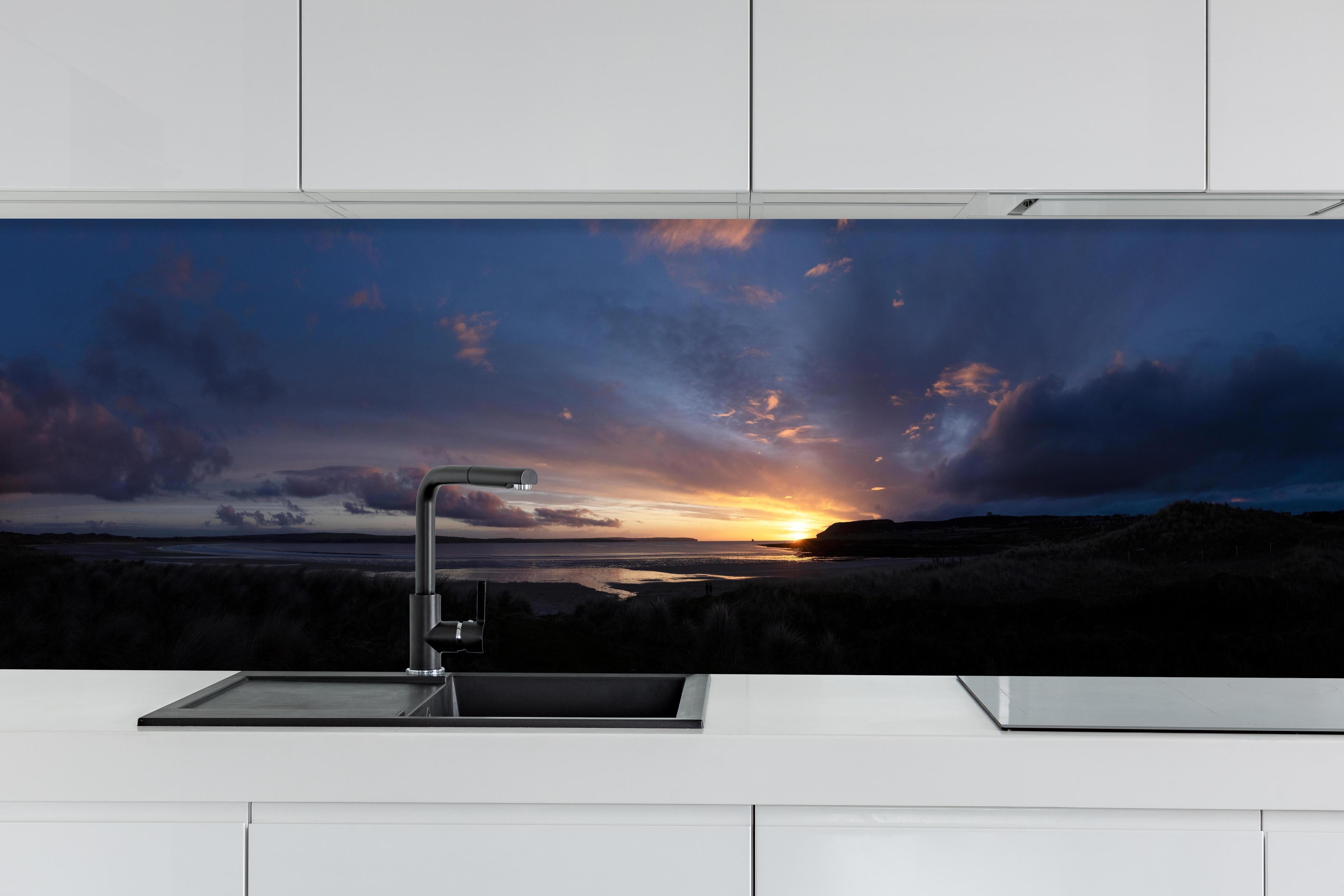 Küche - Ein malerischer Sonnenuntergang über einem ruhigen See, die Wolken leuchten in verschiedenen Blau- und Orangetönen hinter weißen Hochglanz-Küchenregalen und schwarzem Wasserhahn