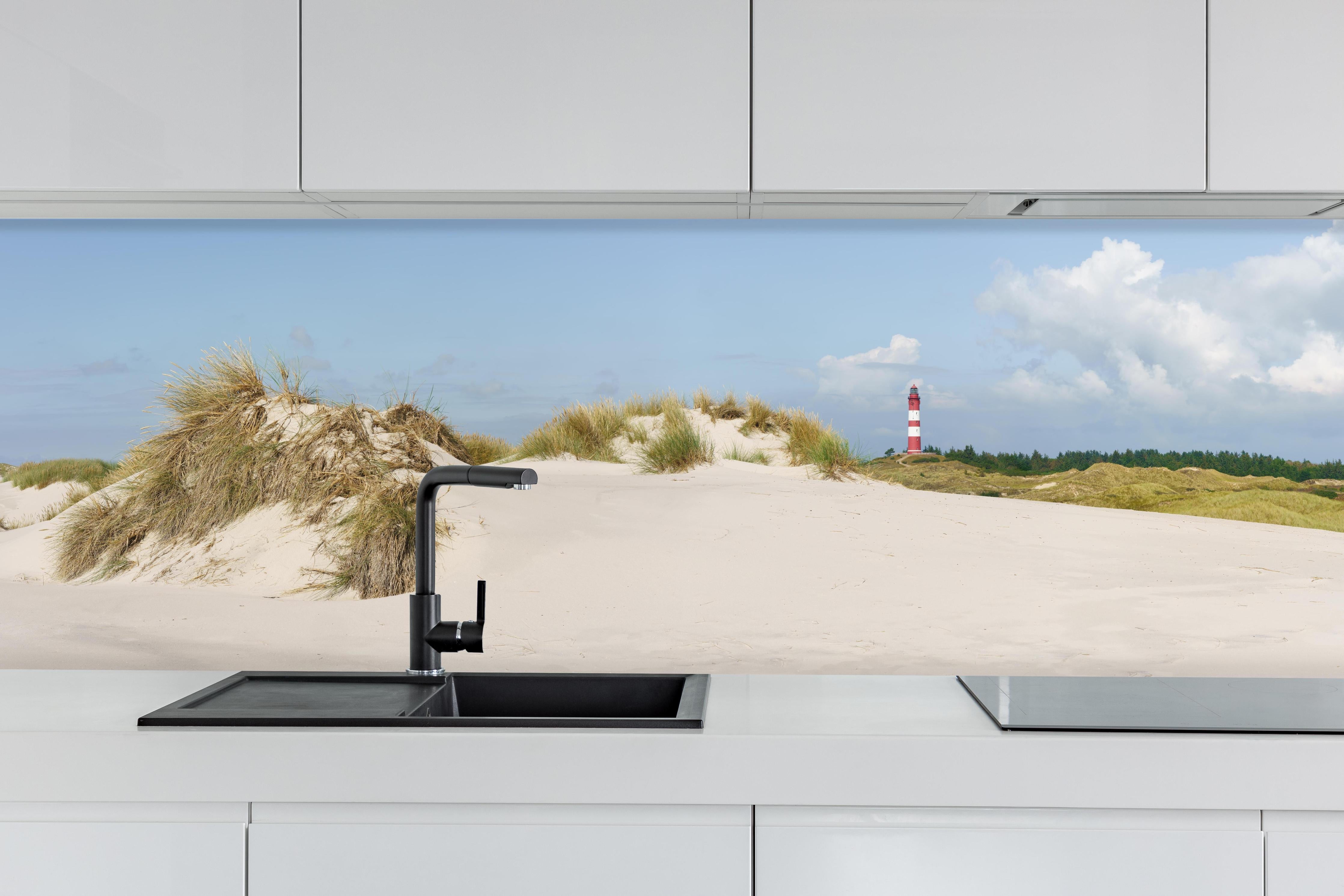 Küche - Ein traumhafter Blick auf die weiße Sanddüne und den roten Leuchtturm am Meer hinter weißen Hochglanz-Küchenregalen und schwarzem Wasserhahn