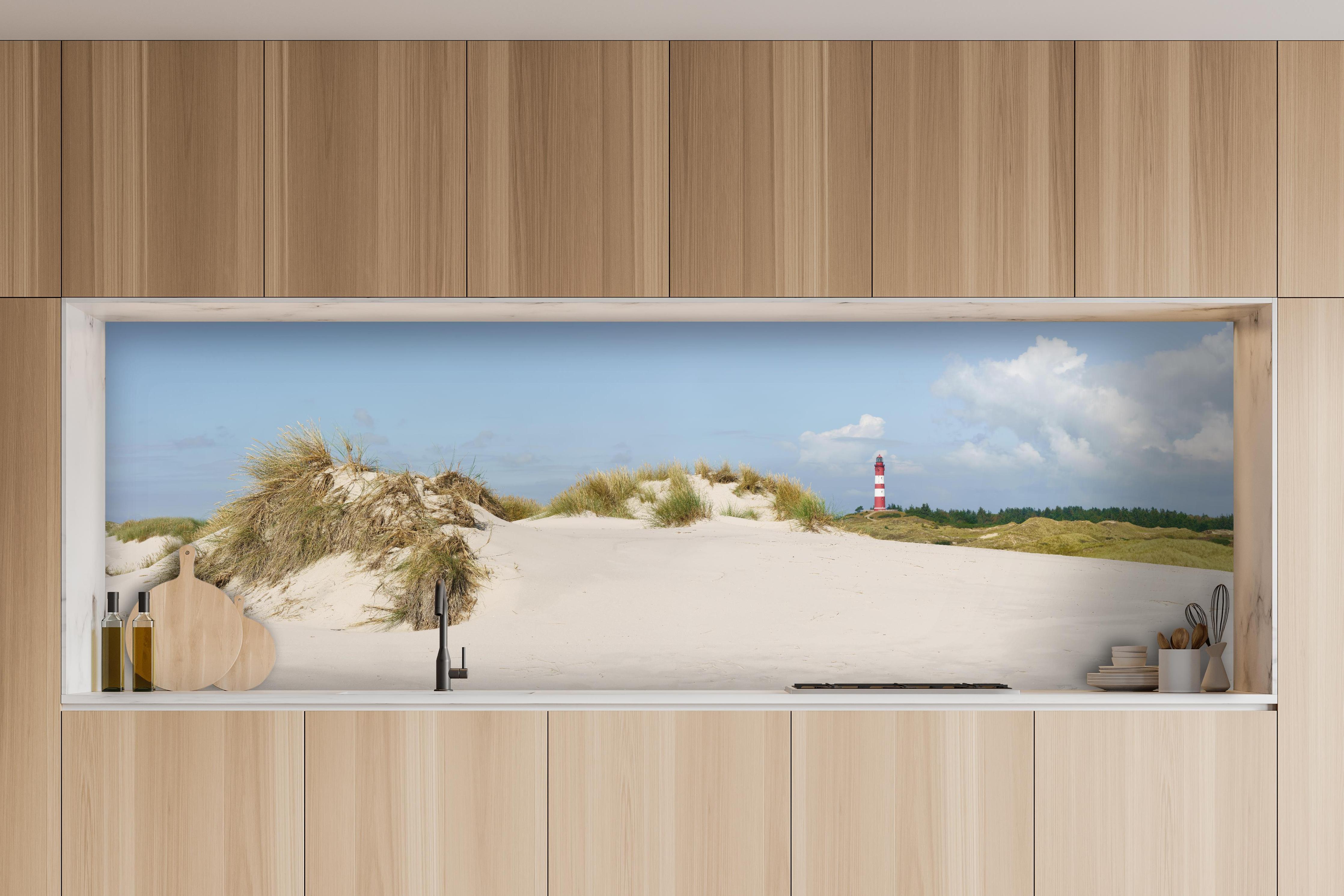 Küche - Ein traumhafter Blick auf die weiße Sanddüne und den roten Leuchtturm am Meer hinter weißen Hochglanz-Küchenregalen und schwarzem Wasserhahn