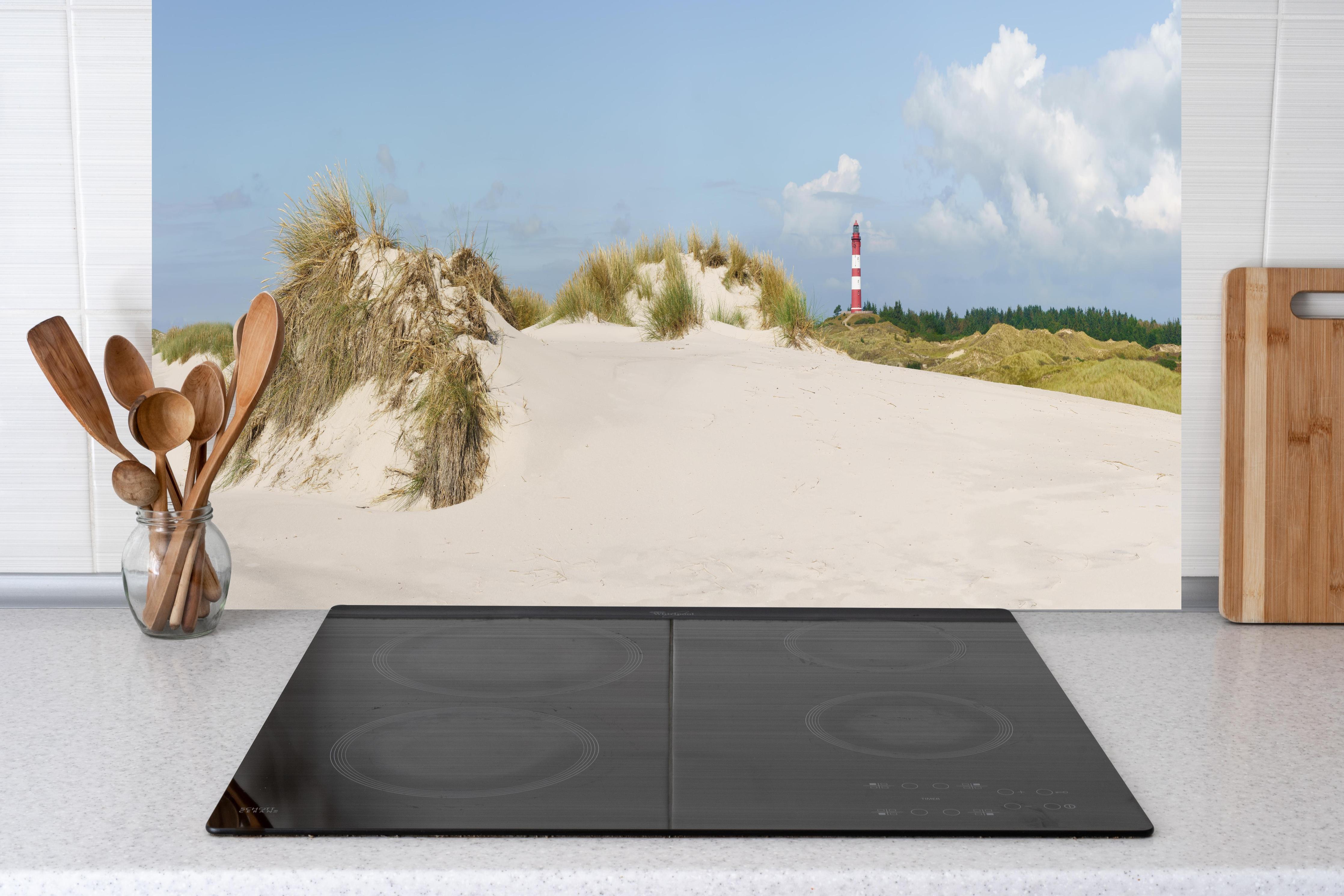 Küche - Ein traumhafter Blick auf die weiße Sanddüne und den roten Leuchtturm am Meer hinter weißen Hochglanz-Küchenregalen und schwarzem Wasserhahn