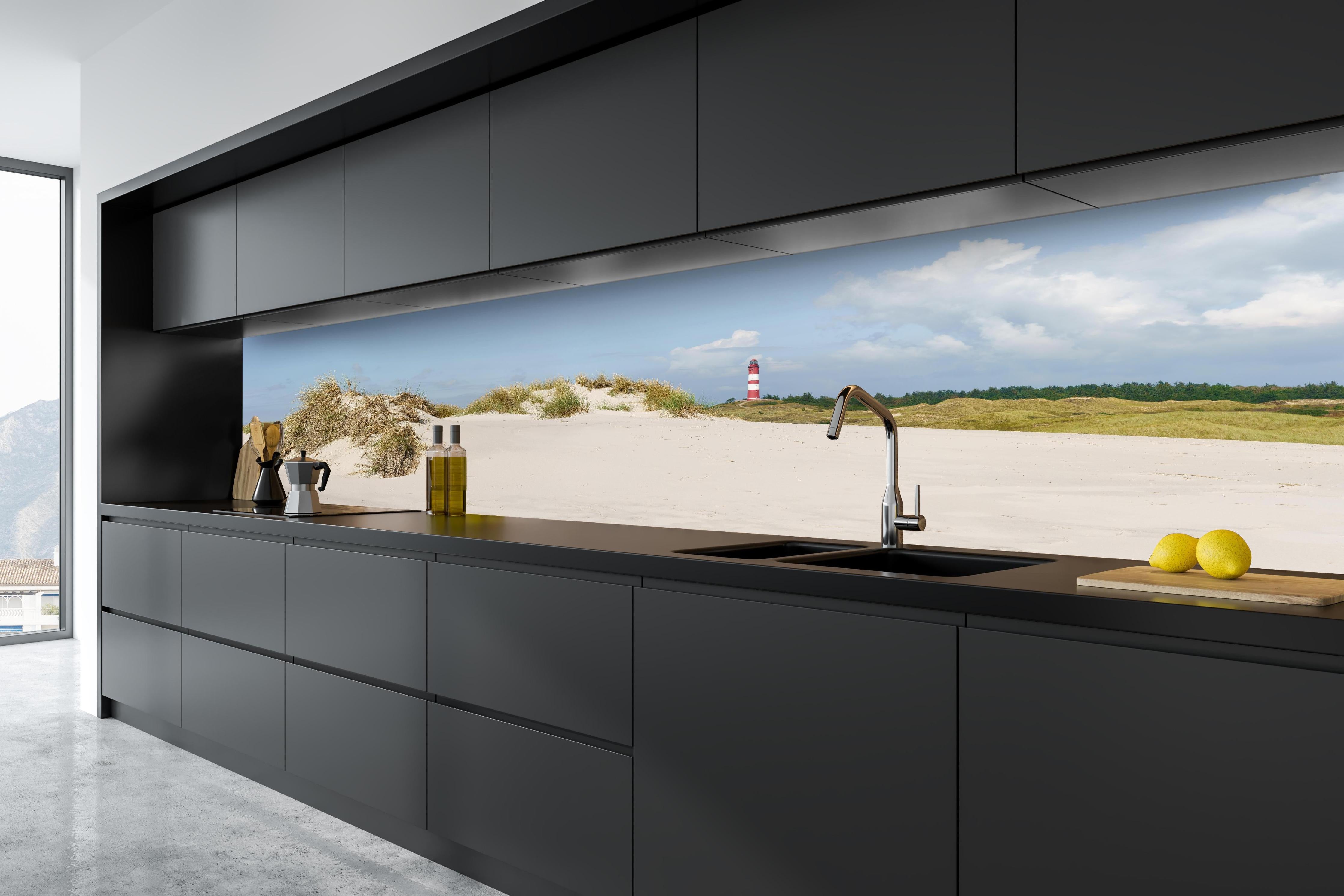 Küche - Ein traumhafter Blick auf die weiße Sanddüne und den roten Leuchtturm am Meer hinter weißen Hochglanz-Küchenregalen und schwarzem Wasserhahn