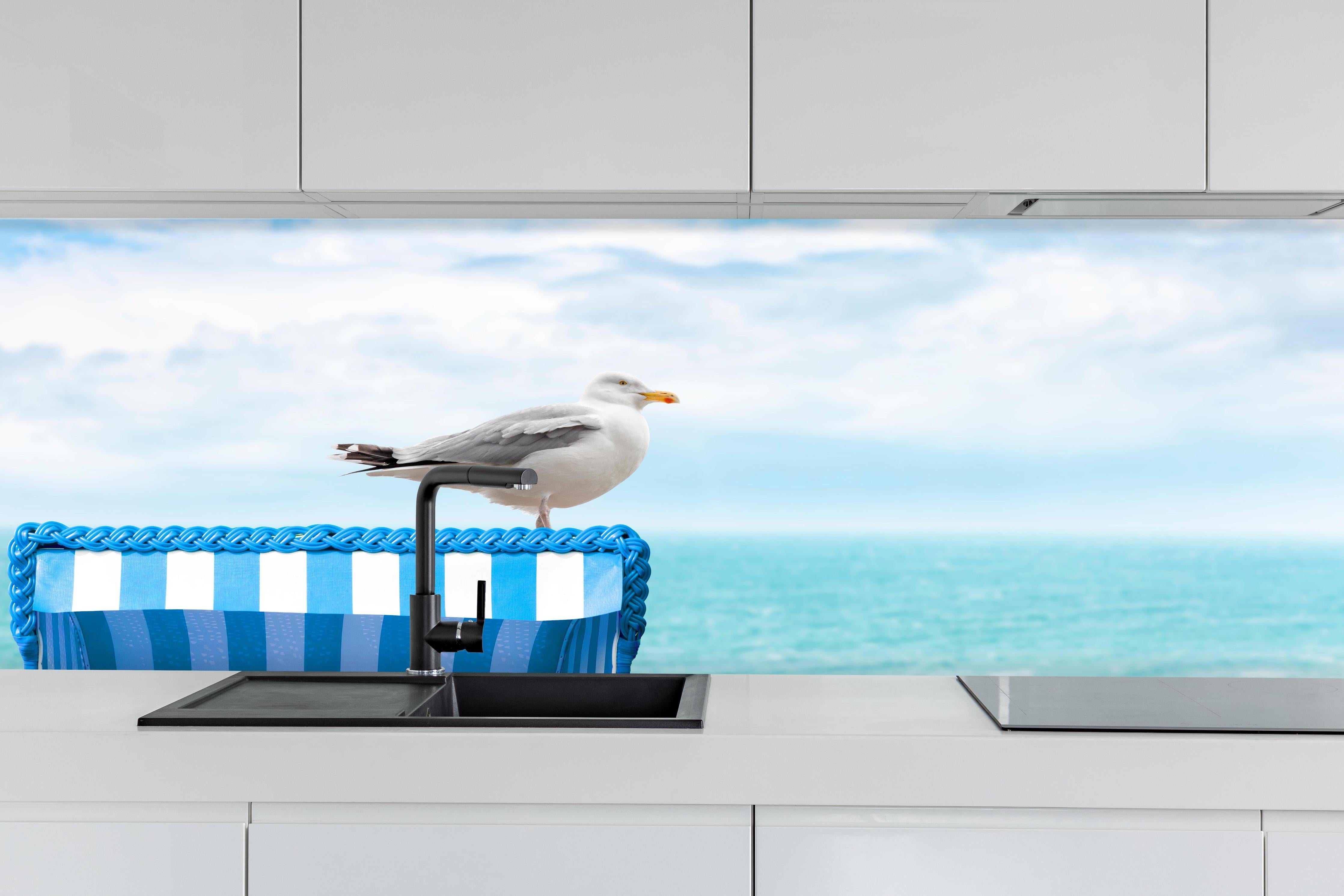 Küche - Elegant Seagull Perched on Blue Beach Chair by the Tranquil Ocean hinter weißen Hochglanz-Küchenregalen und schwarzem Wasserhahn