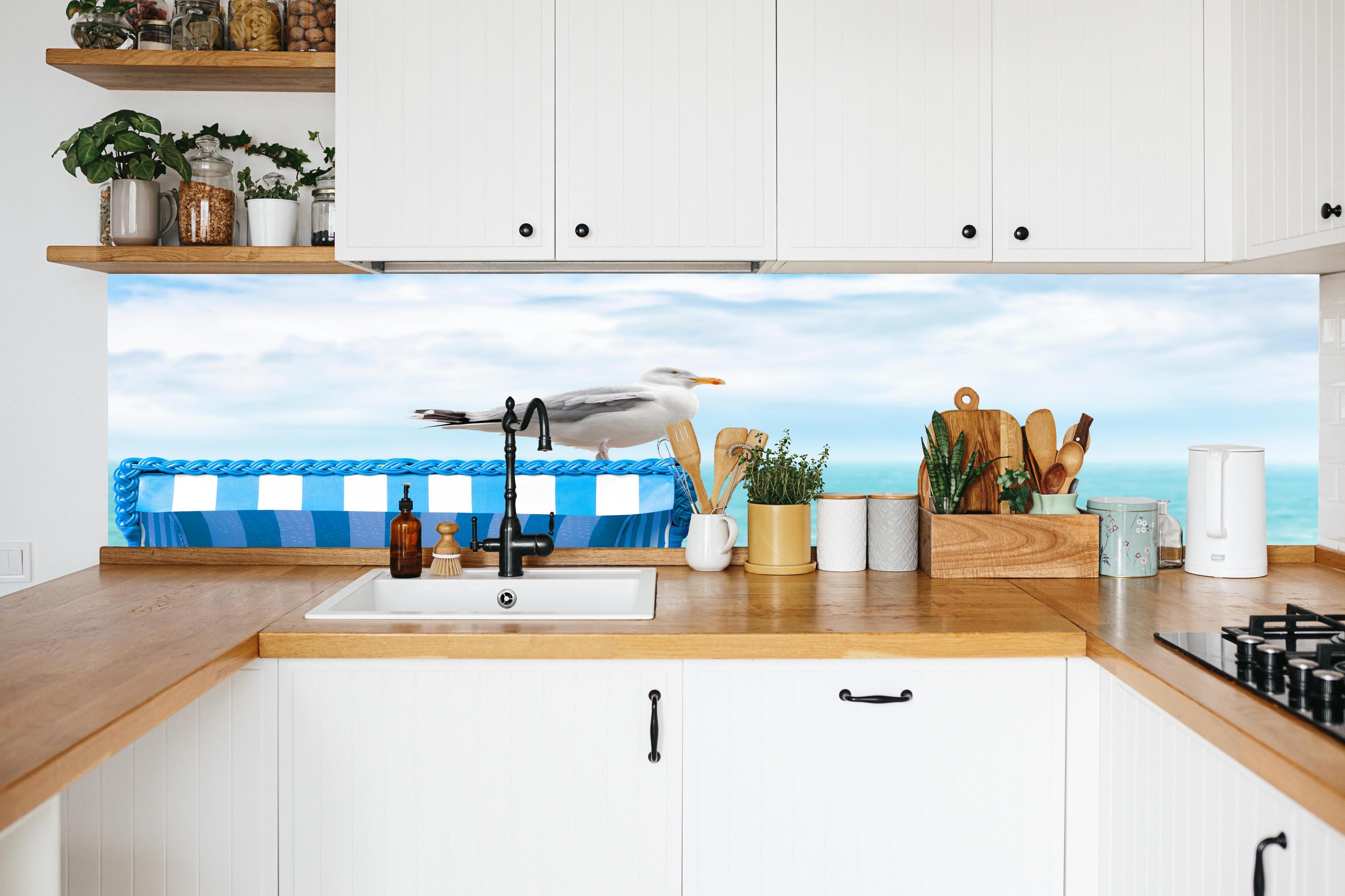 Küche - Elegant Seagull Perched on Blue Beach Chair by the Tranquil Ocean hinter weißen Hochglanz-Küchenregalen und schwarzem Wasserhahn