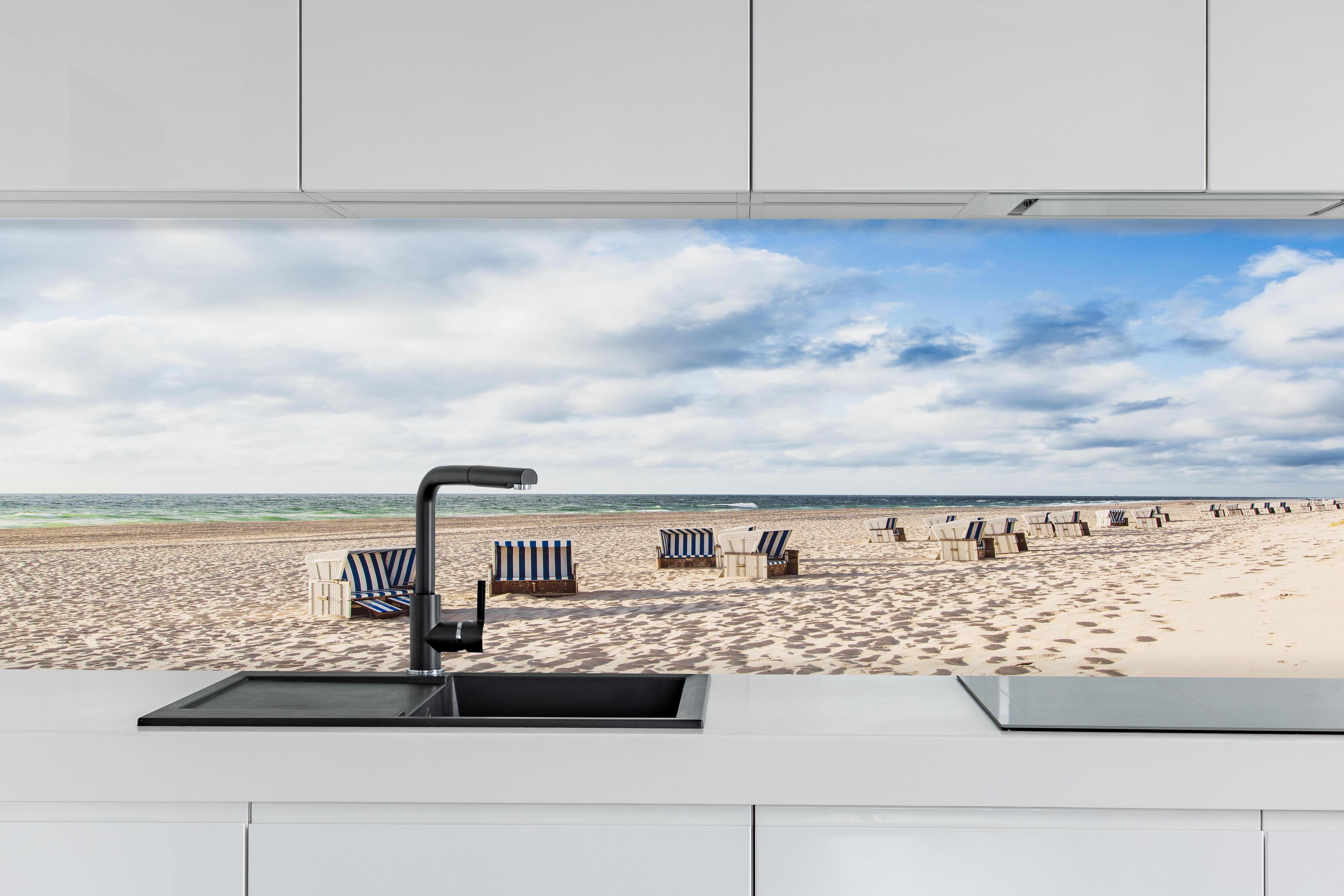 Küche - Entspannte Strandatmosphäre mit blauen und weißen Liegestühlen am Meer hinter weißen Hochglanz-Küchenregalen und schwarzem Wasserhahn