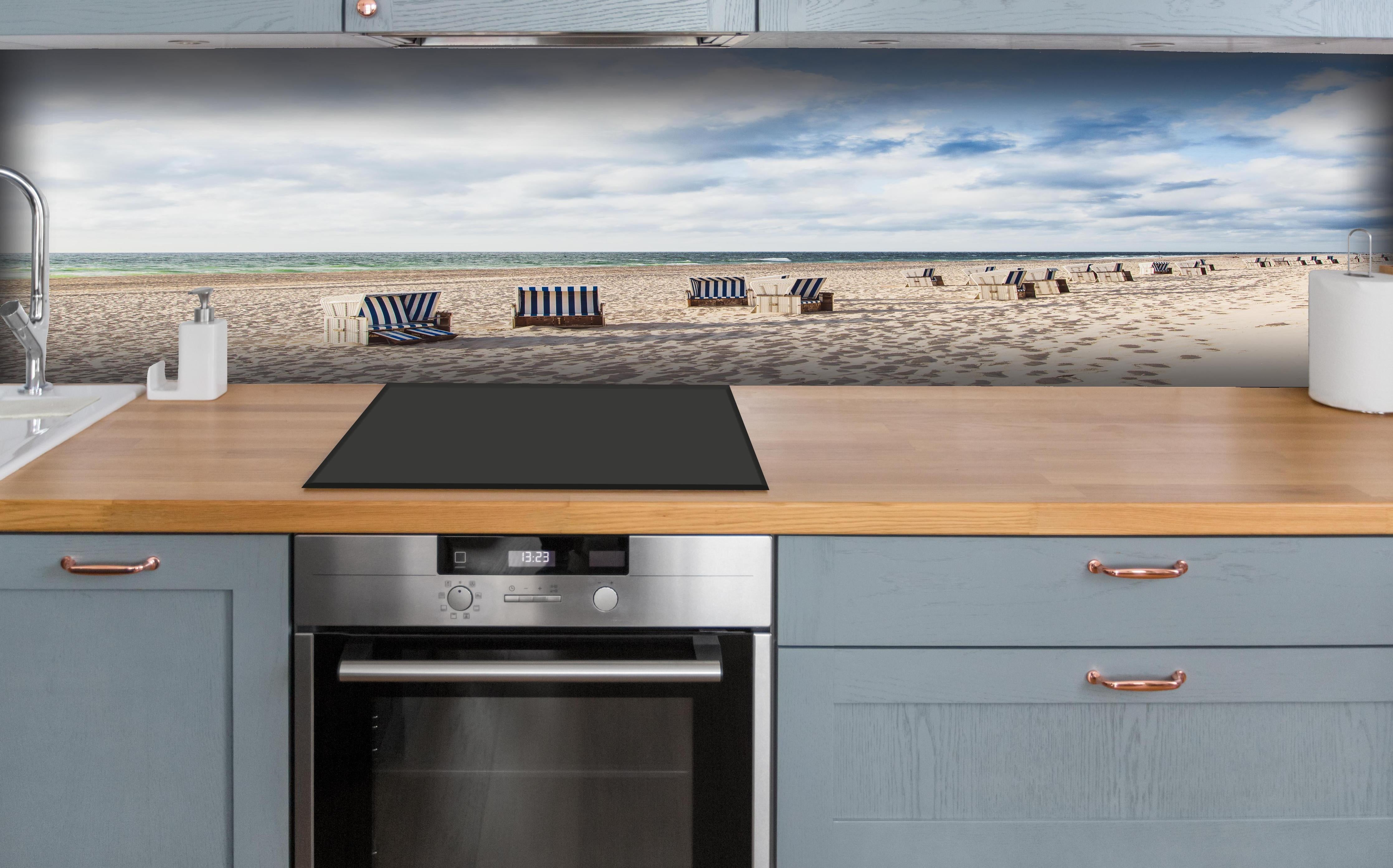 Küche - Entspannte Strandatmosphäre mit blauen und weißen Liegestühlen am Meer hinter weißen Hochglanz-Küchenregalen und schwarzem Wasserhahn