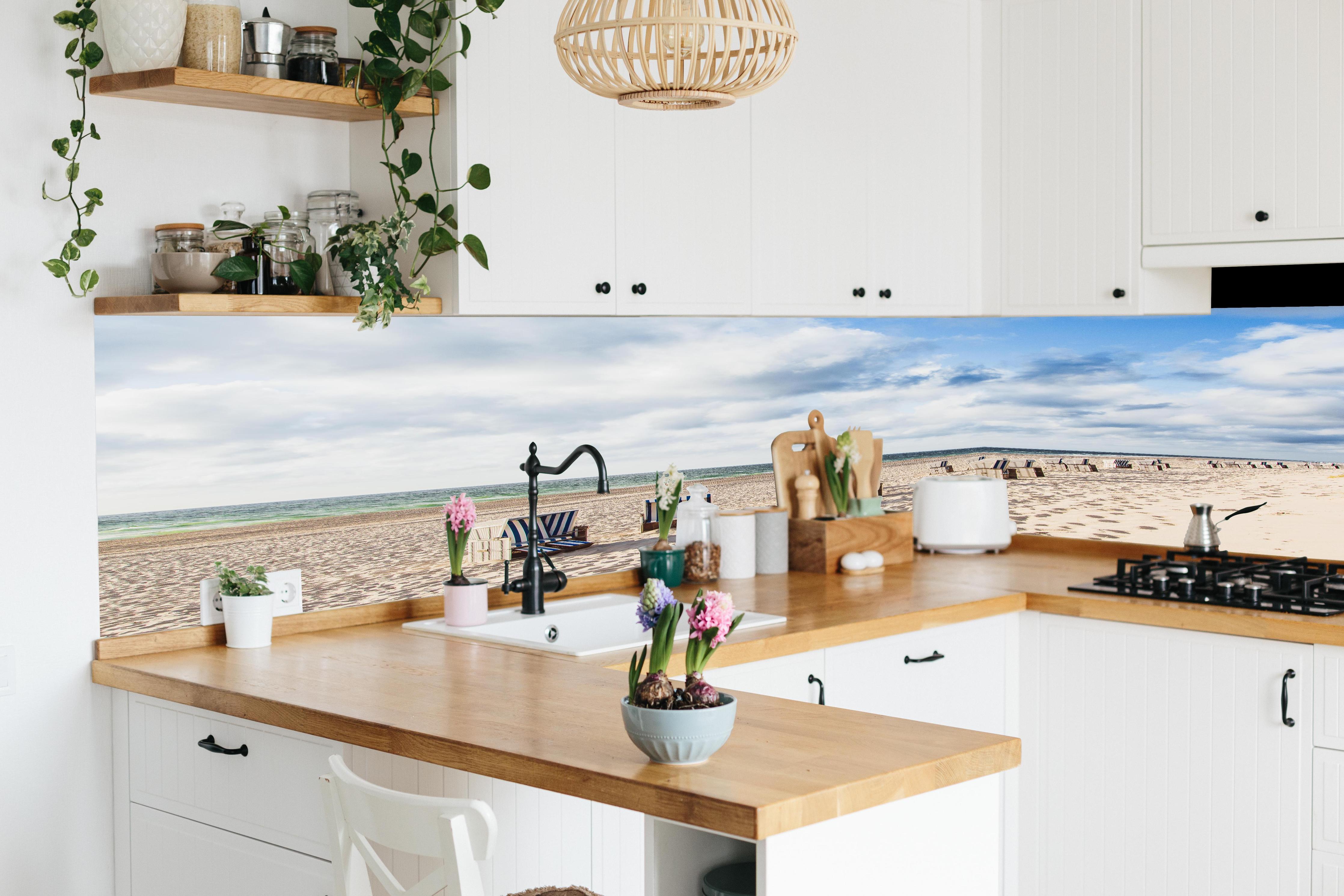 Küche - Entspannte Strandatmosphäre mit blauen und weißen Liegestühlen am Meer hinter weißen Hochglanz-Küchenregalen und schwarzem Wasserhahn