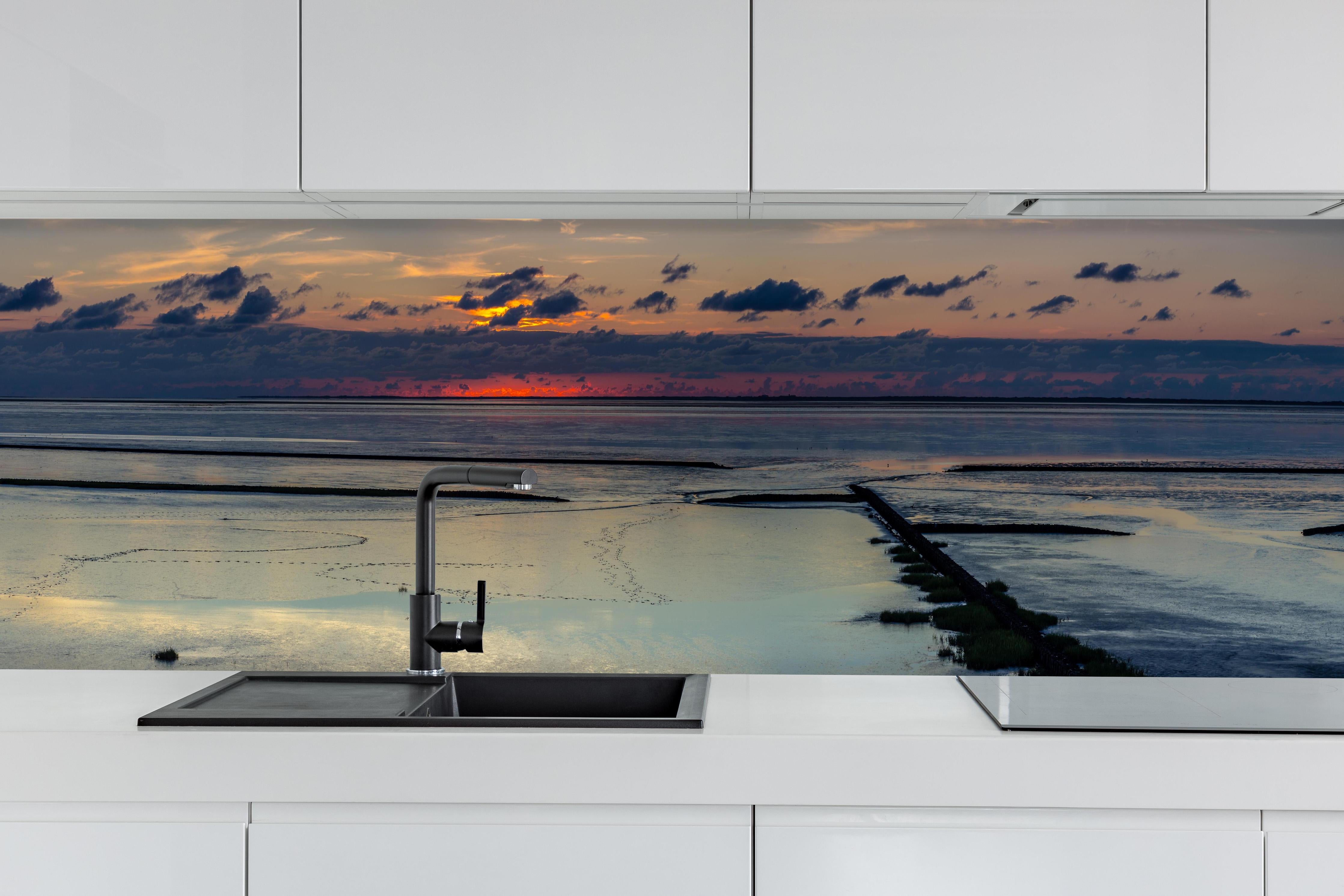 Küche - Faszinierender Sonnenuntergang über einem stillen Gewässer hinter weißen Hochglanz-Küchenregalen und schwarzem Wasserhahn