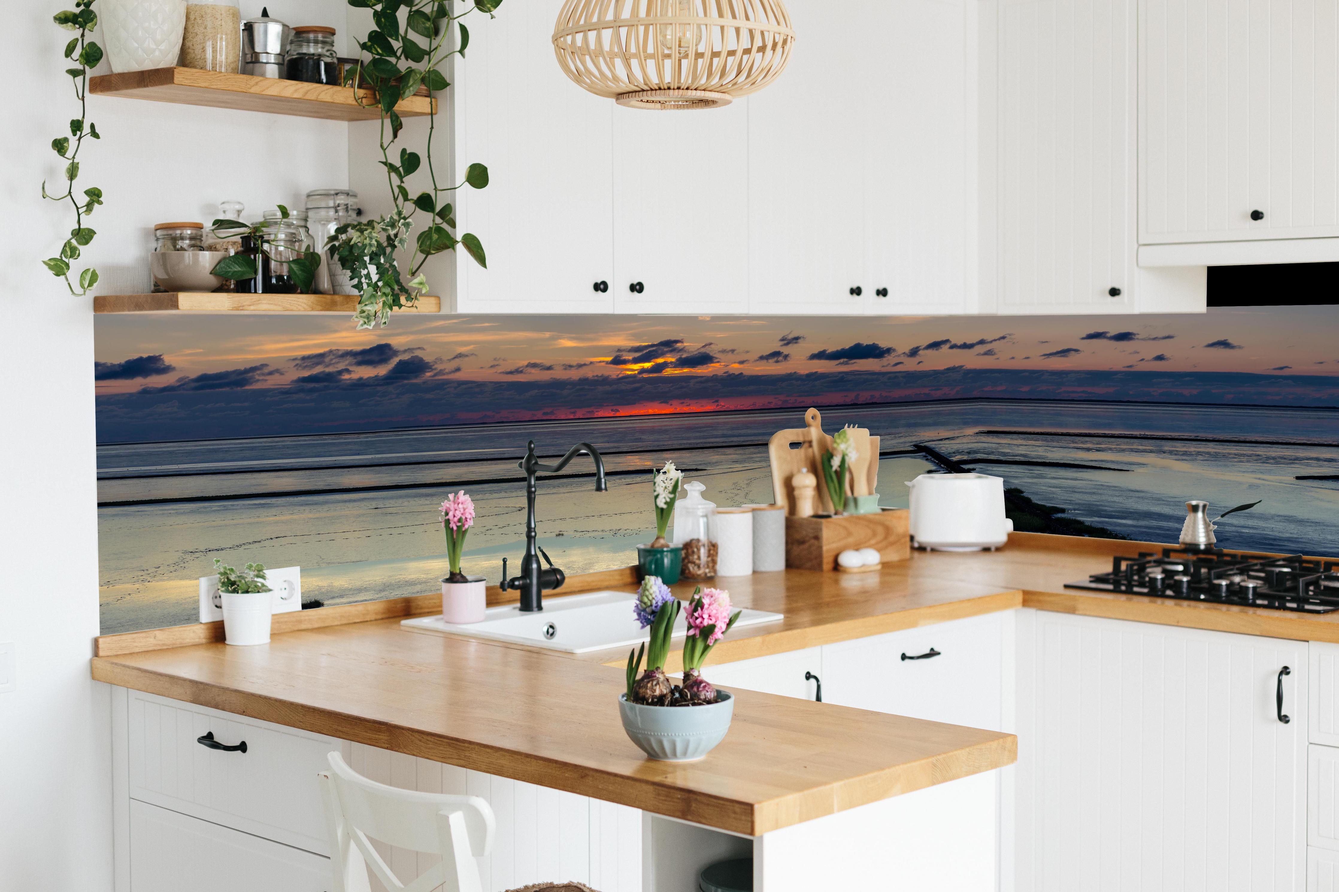 Küche - Faszinierender Sonnenuntergang über einem stillen Gewässer hinter weißen Hochglanz-Küchenregalen und schwarzem Wasserhahn