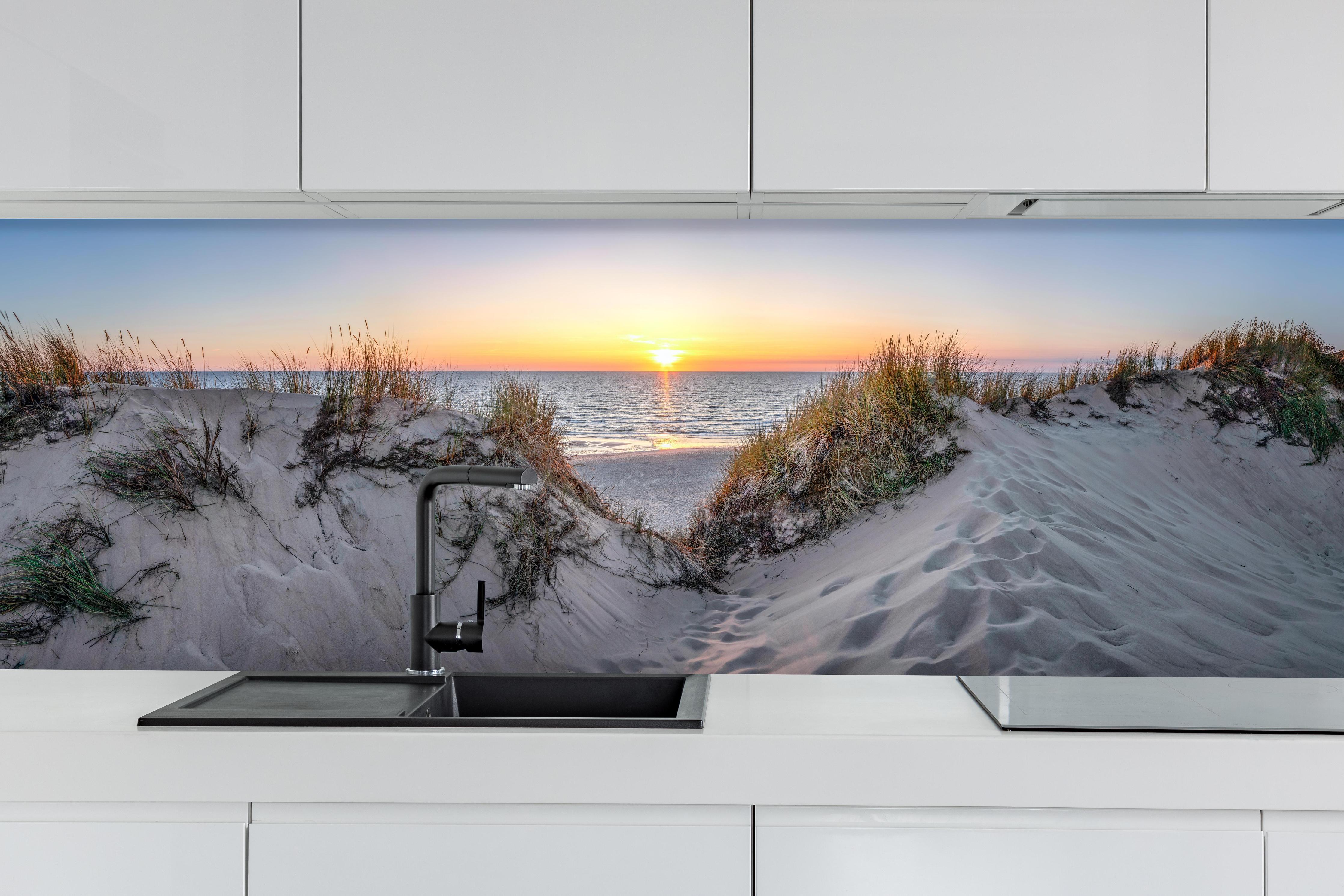 Küche - Faszinierender Sonnenuntergang über einer Sanddüne am Meer hinter weißen Hochglanz-Küchenregalen und schwarzem Wasserhahn