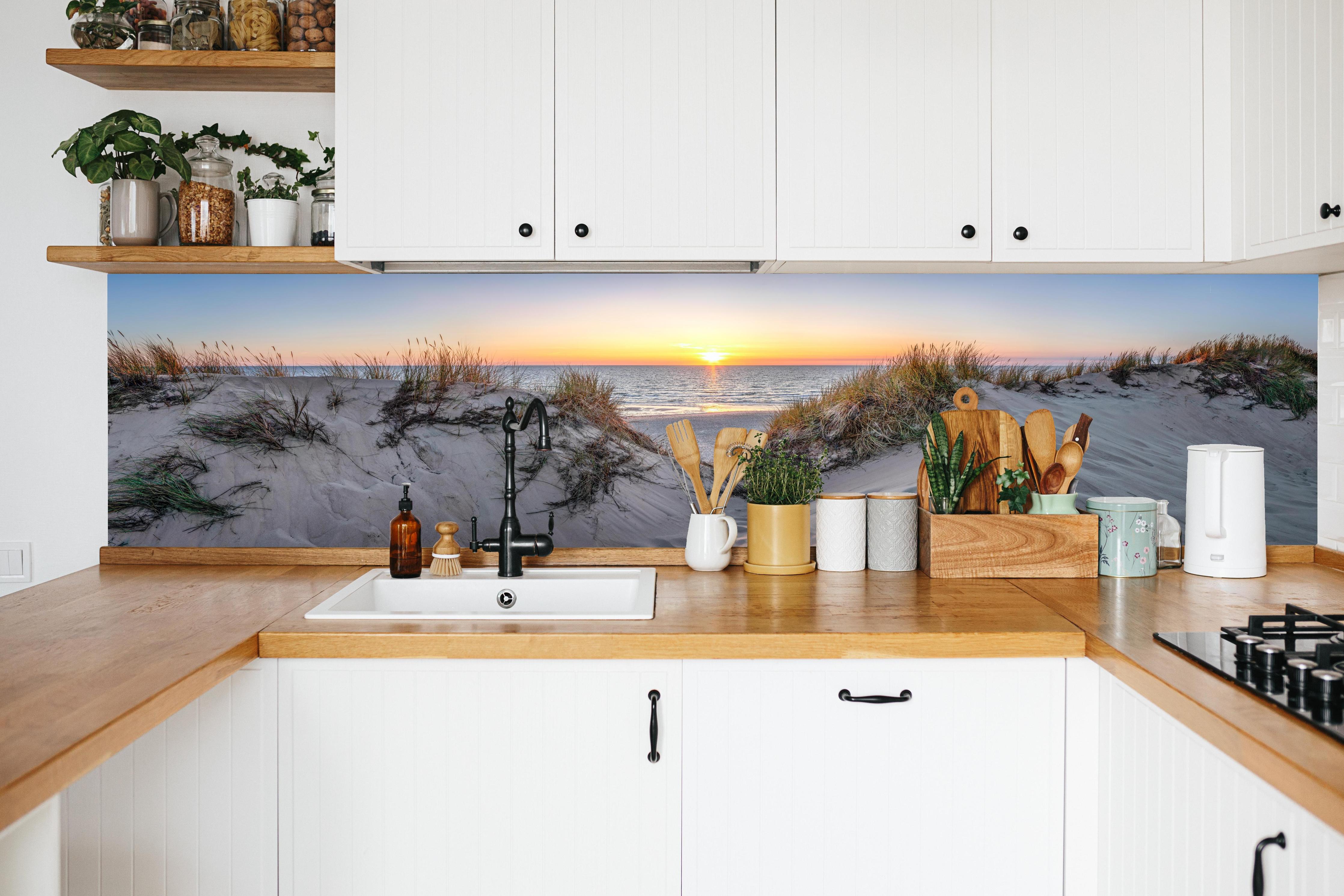 Küche - Faszinierender Sonnenuntergang über einer Sanddüne am Meer hinter weißen Hochglanz-Küchenregalen und schwarzem Wasserhahn