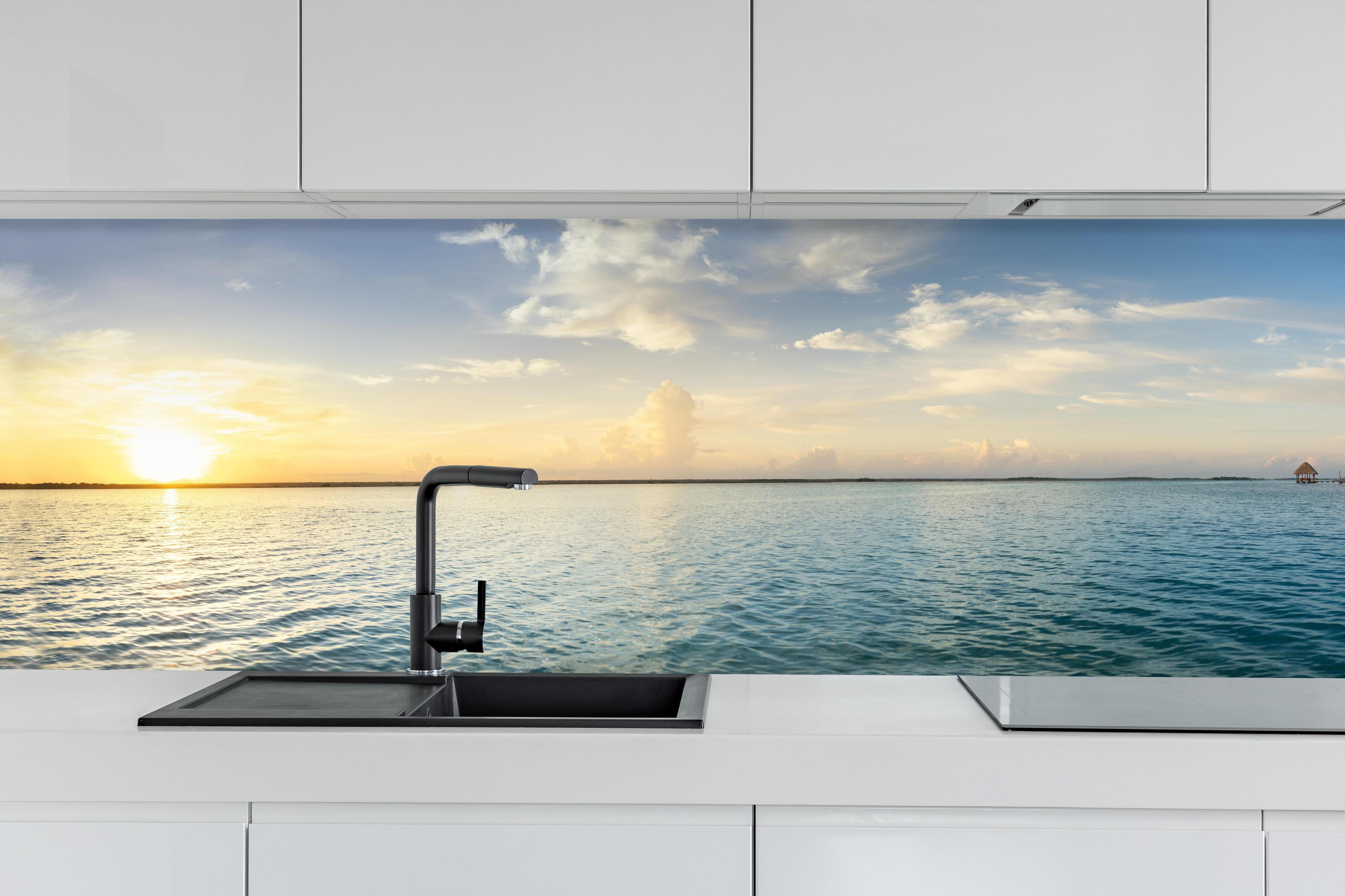 Küche - Faszinierender Sonnenuntergang über glitzerndem Wasser hinter weißen Hochglanz-Küchenregalen und schwarzem Wasserhahn