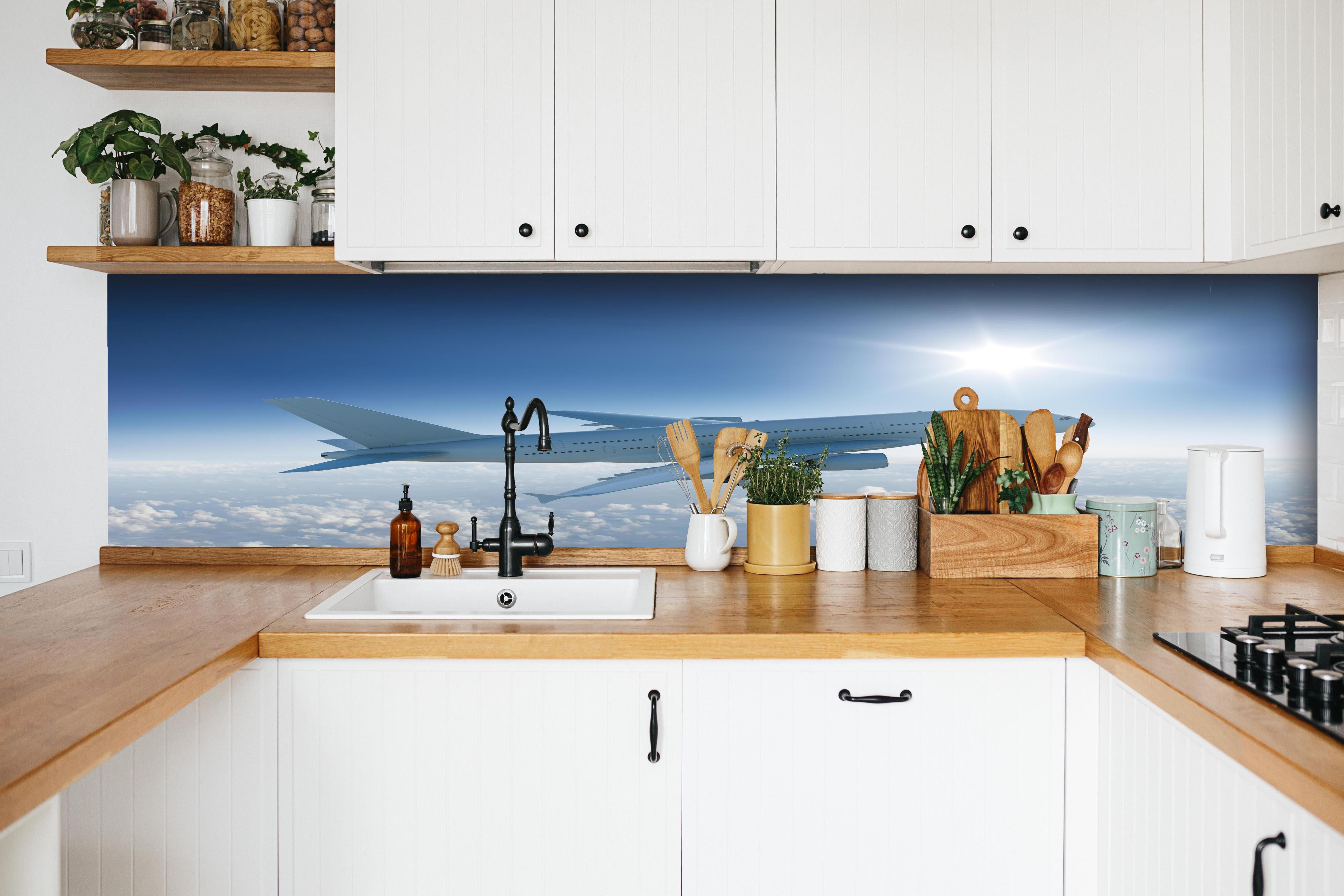 Küche - Flugzeug über weißen Wolken hinter weißen Hochglanz-Küchenregalen und schwarzem Wasserhahn
