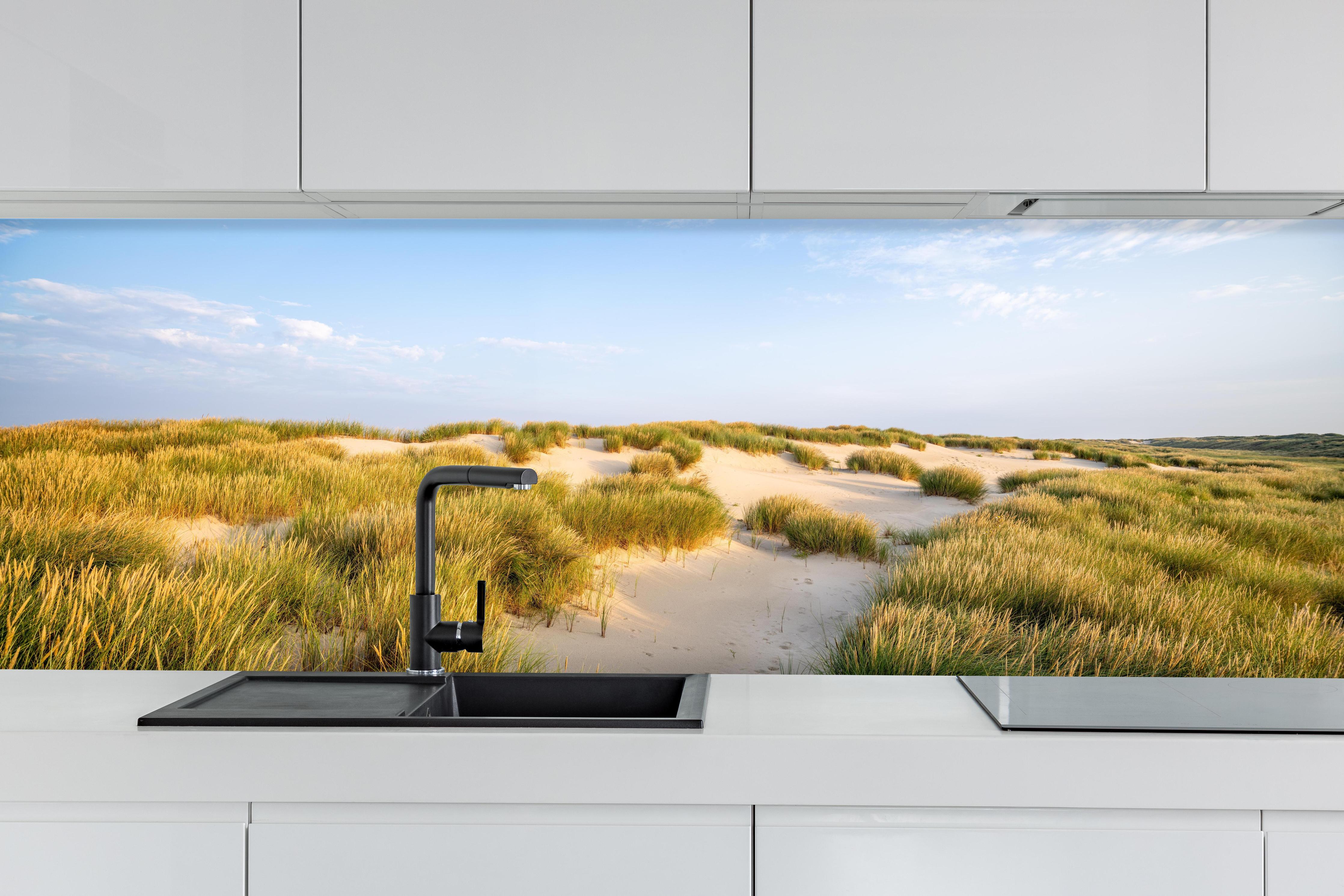 Küche - Friedliche Dünenlandschaft mit leuchtendem Gras im warmen Sonnenlicht hinter weißen Hochglanz-Küchenregalen und schwarzem Wasserhahn