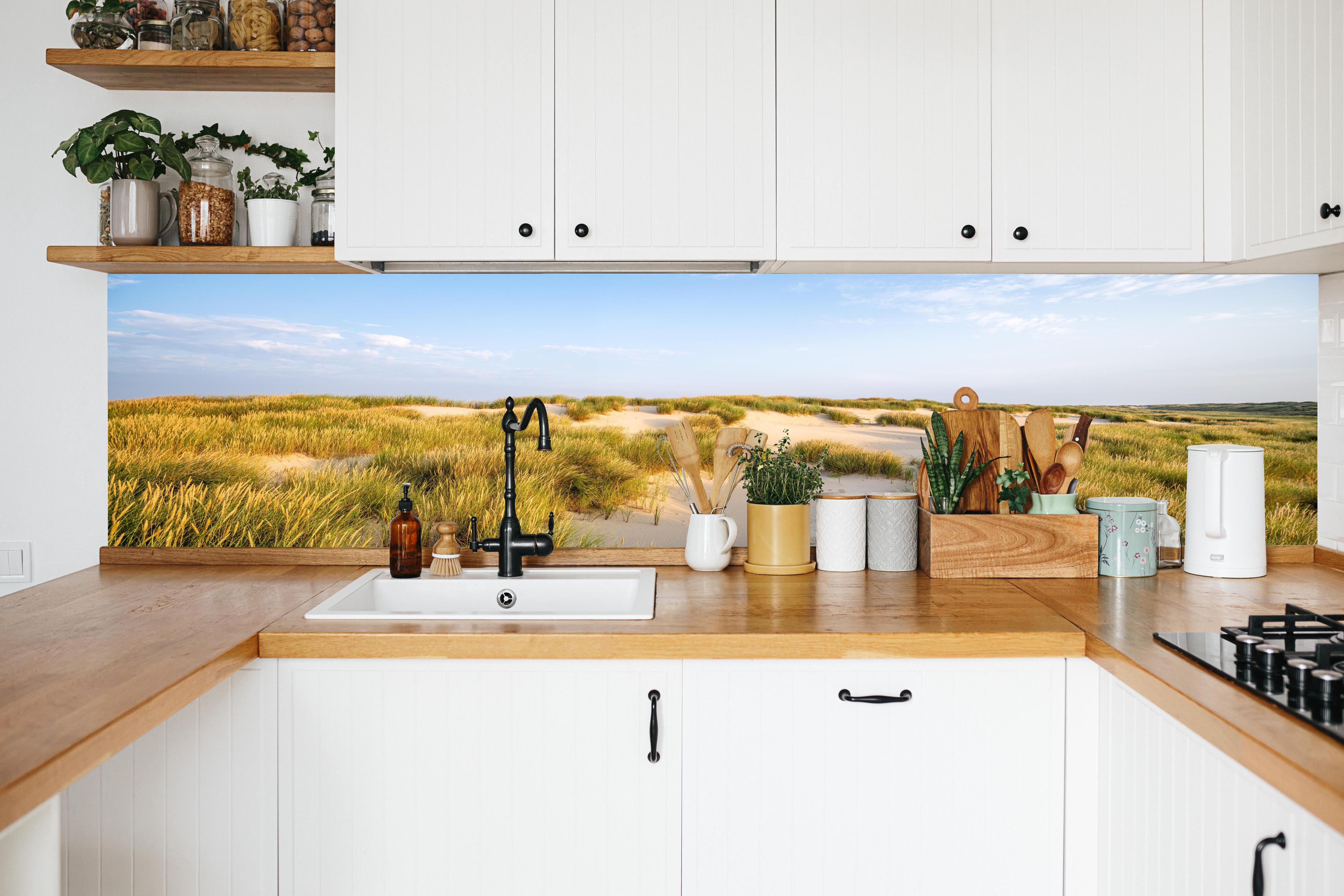 Küche - Friedliche Dünenlandschaft mit leuchtendem Gras im warmen Sonnenlicht hinter weißen Hochglanz-Küchenregalen und schwarzem Wasserhahn