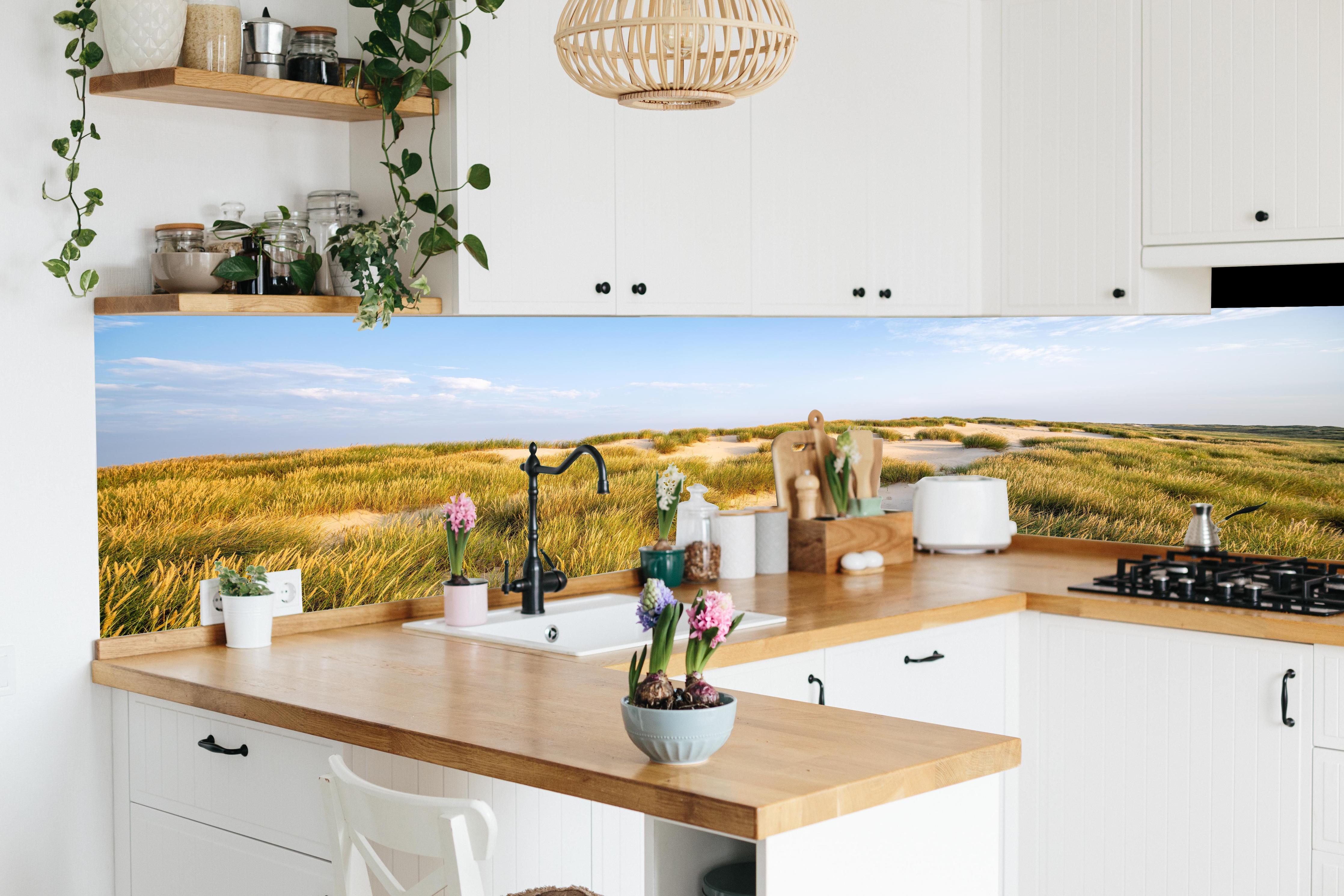 Küche - Friedliche Dünenlandschaft mit leuchtendem Gras im warmen Sonnenlicht hinter weißen Hochglanz-Küchenregalen und schwarzem Wasserhahn