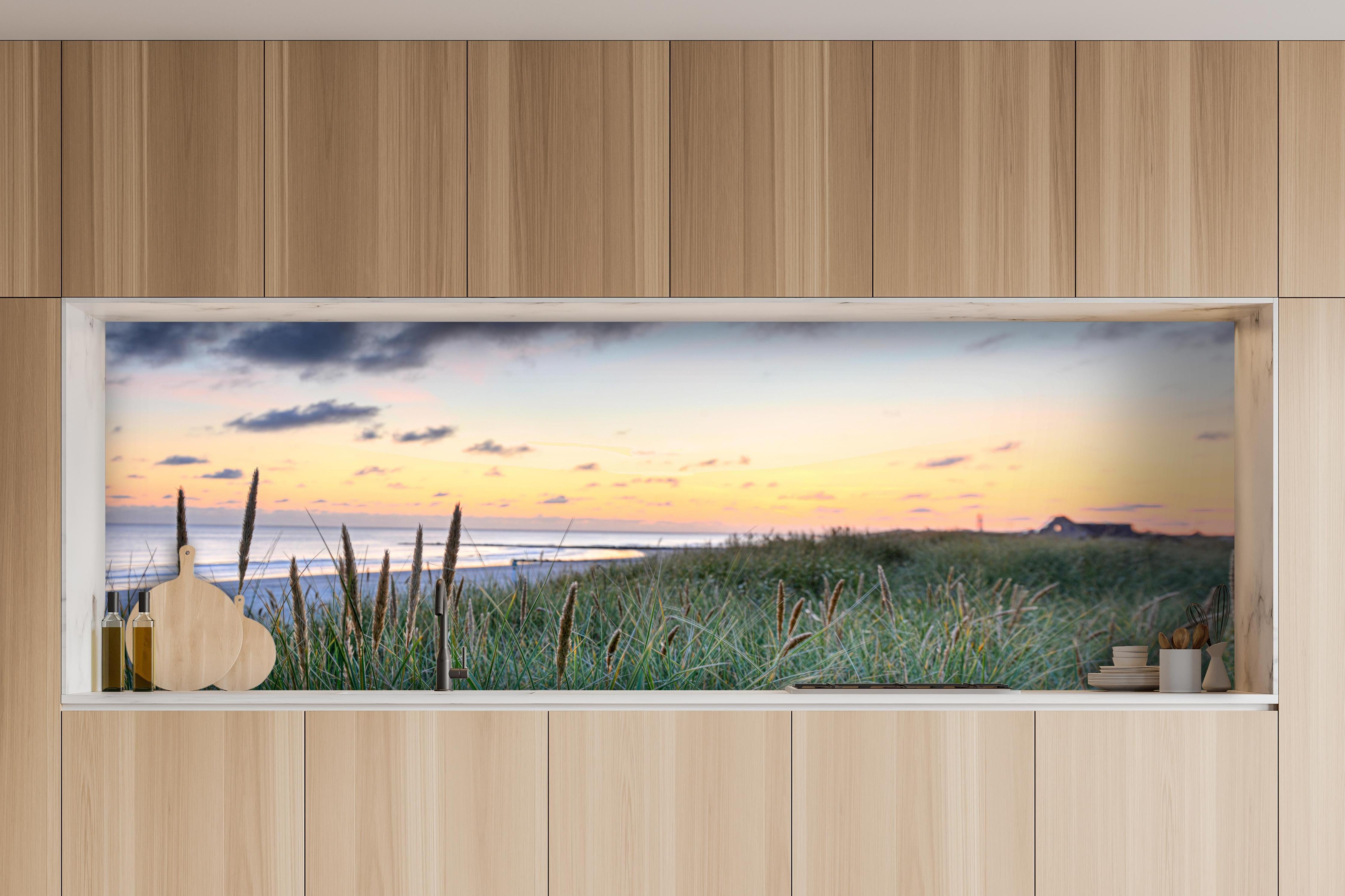 Küche - Friedliche Strandlandschaft mit grünem Gras und sanften Wellen bei Sonnenuntergang hinter weißen Hochglanz-Küchenregalen und schwarzem Wasserhahn