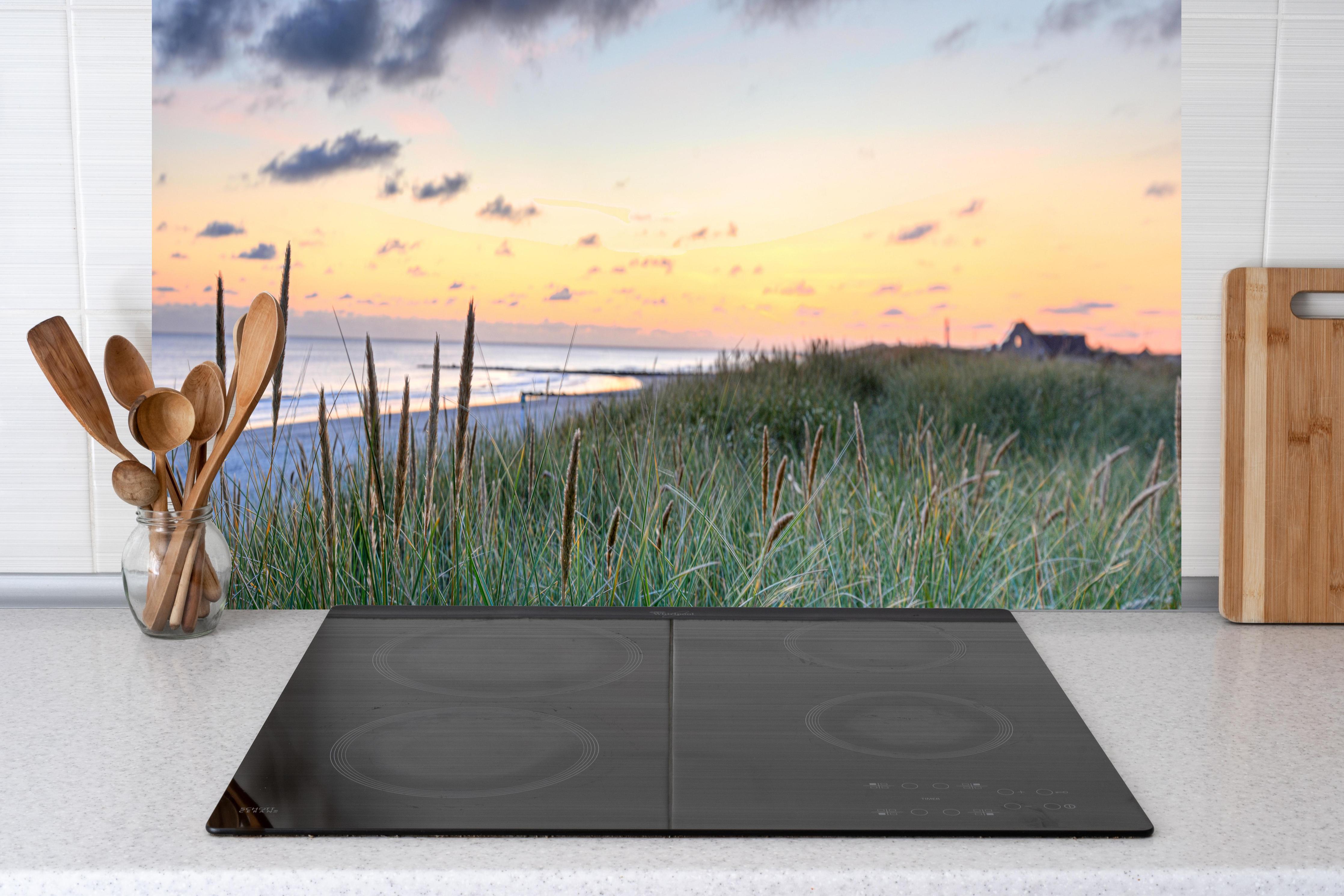 Küche - Friedliche Strandlandschaft mit grünem Gras und sanften Wellen bei Sonnenuntergang hinter weißen Hochglanz-Küchenregalen und schwarzem Wasserhahn