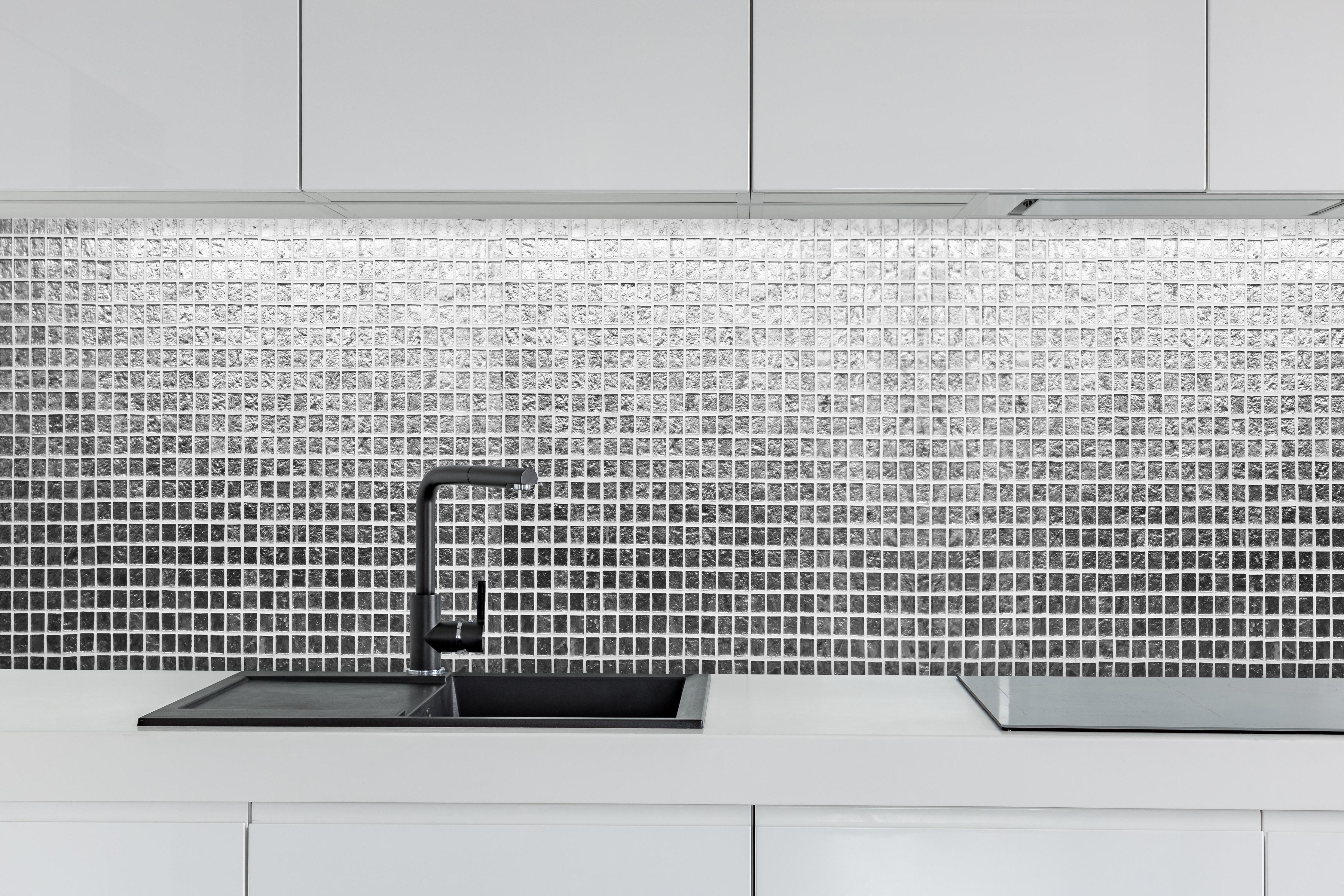 Küche - Glänzende Silberne Fliesen Textur Wand hinter weißen Hochglanz-Küchenregalen und schwarzem Wasserhahn