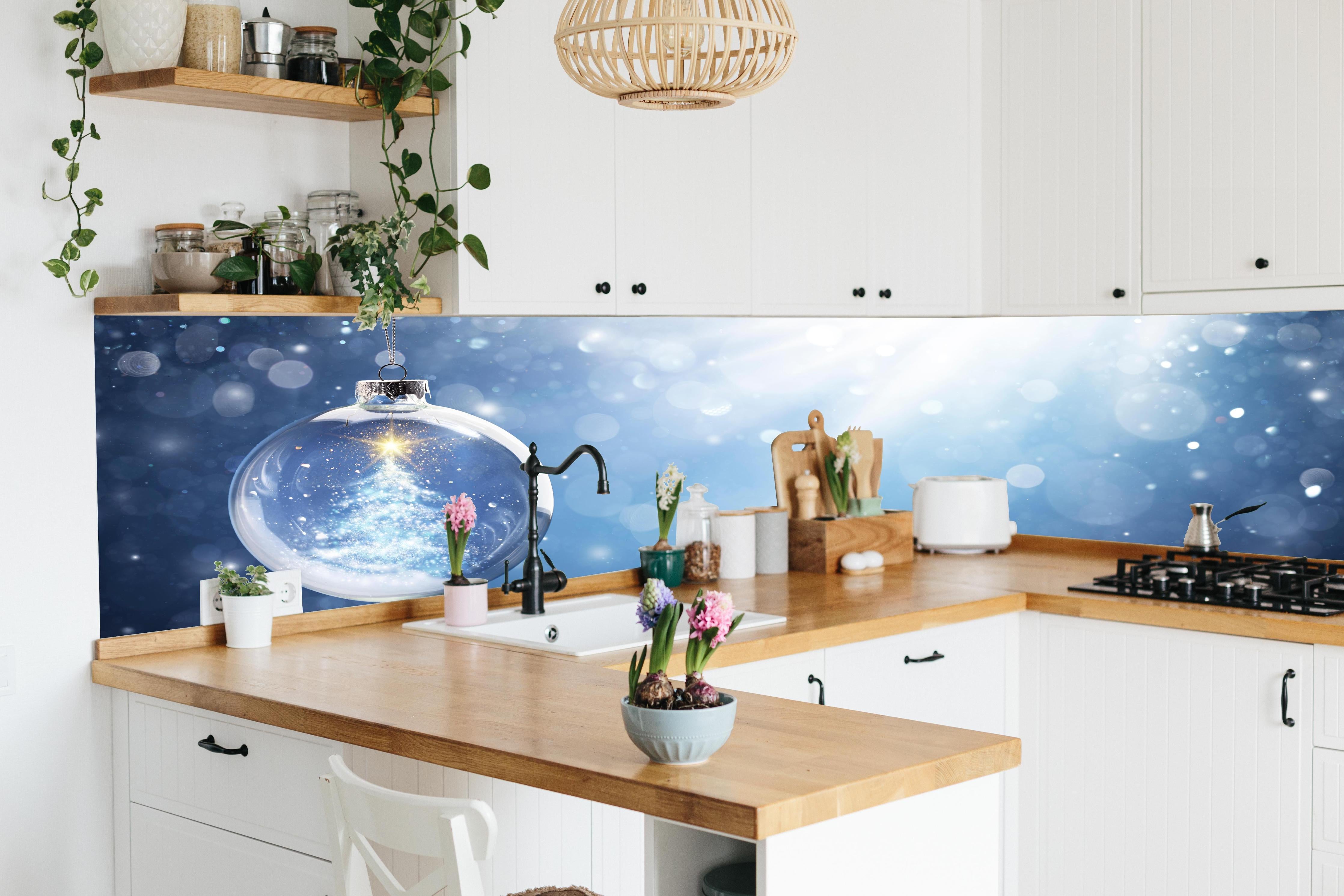 Küche - Glänzender Weihnachtsbaum in Schneekugel hinter weißen Hochglanz-Küchenregalen und schwarzem Wasserhahn