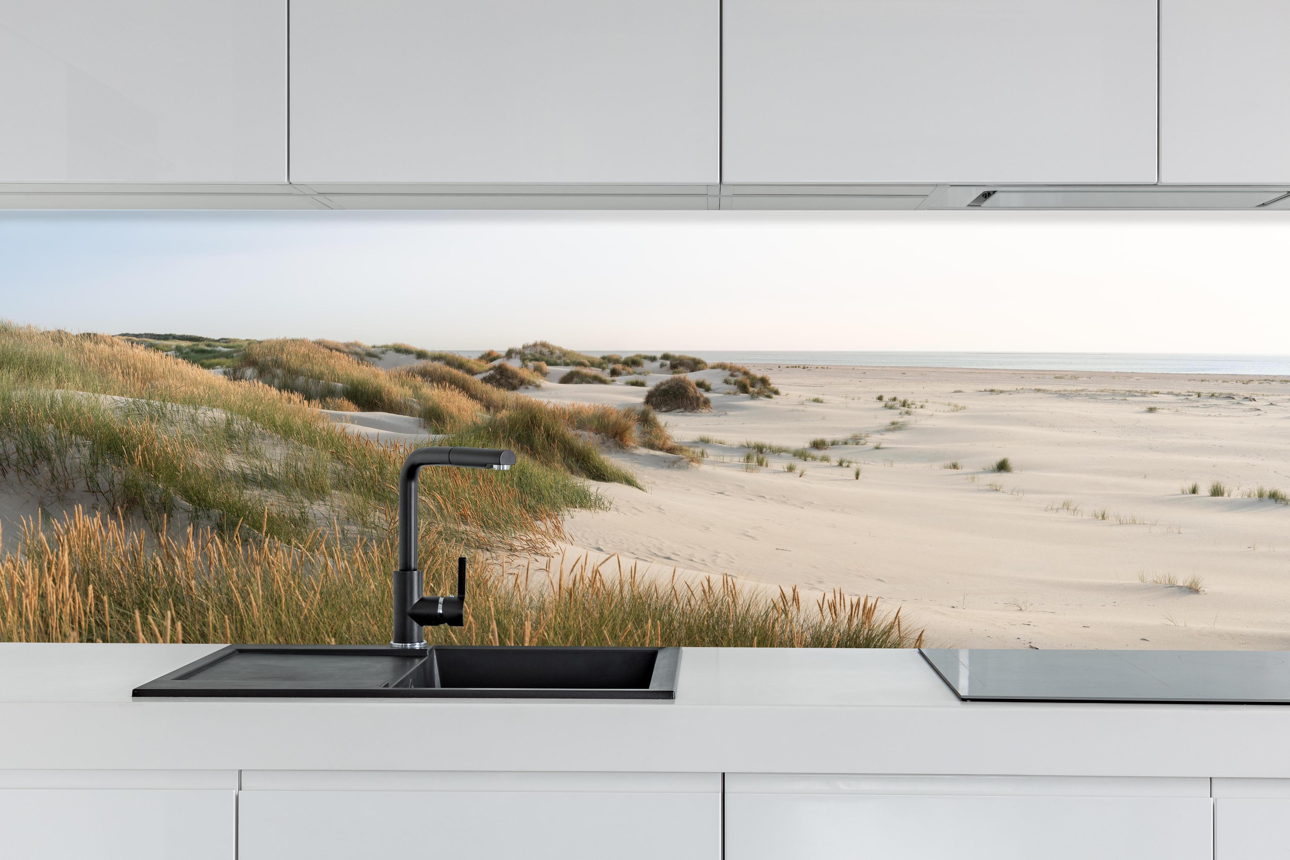 Küche - Harmonische Strandlandschaft mit sanften Sanddünen und Strandgräsern hinter weißen Hochglanz-Küchenregalen und schwarzem Wasserhahn