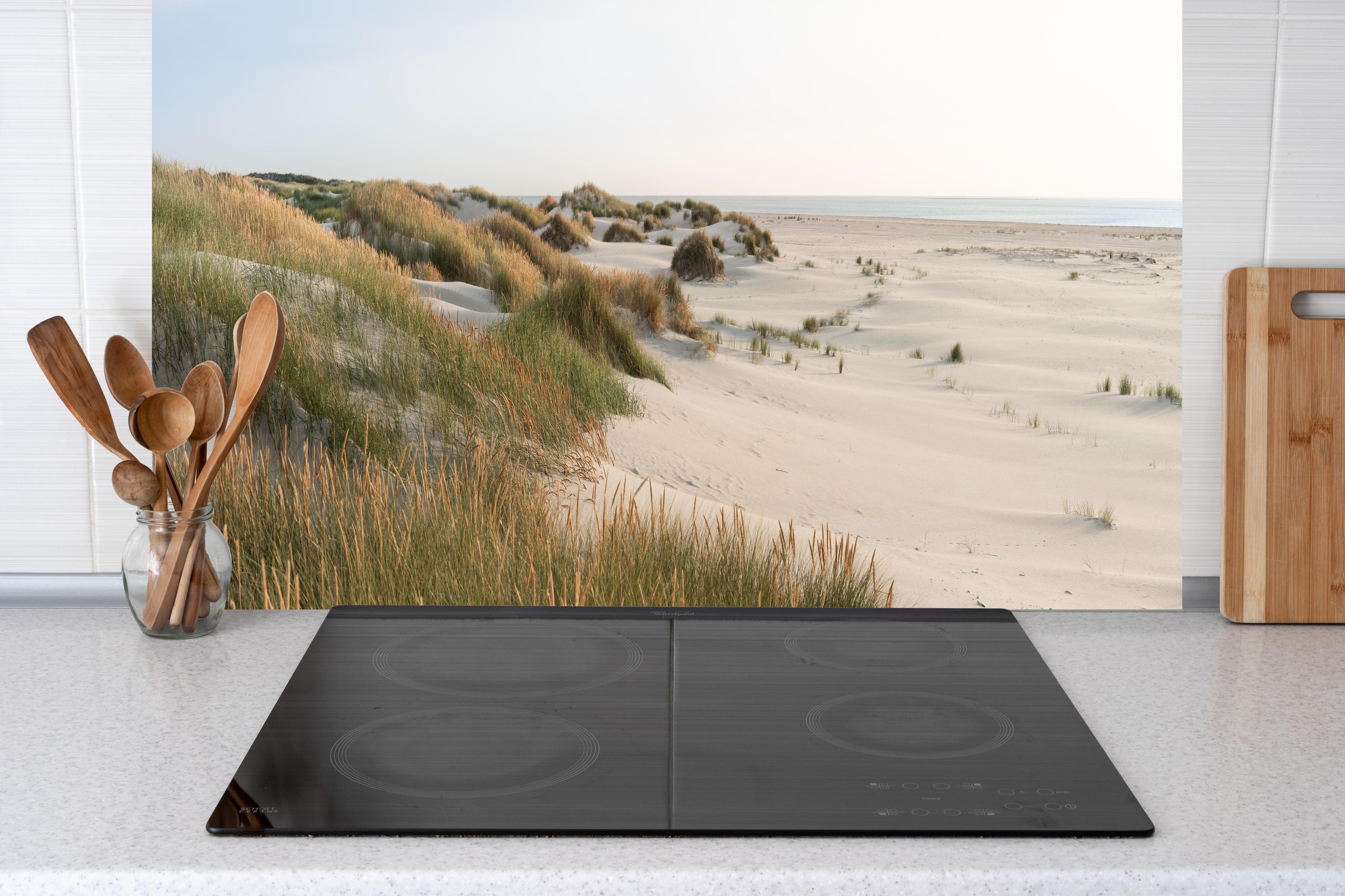 Küche - Harmonische Strandlandschaft mit sanften Sanddünen und Strandgräsern hinter weißen Hochglanz-Küchenregalen und schwarzem Wasserhahn