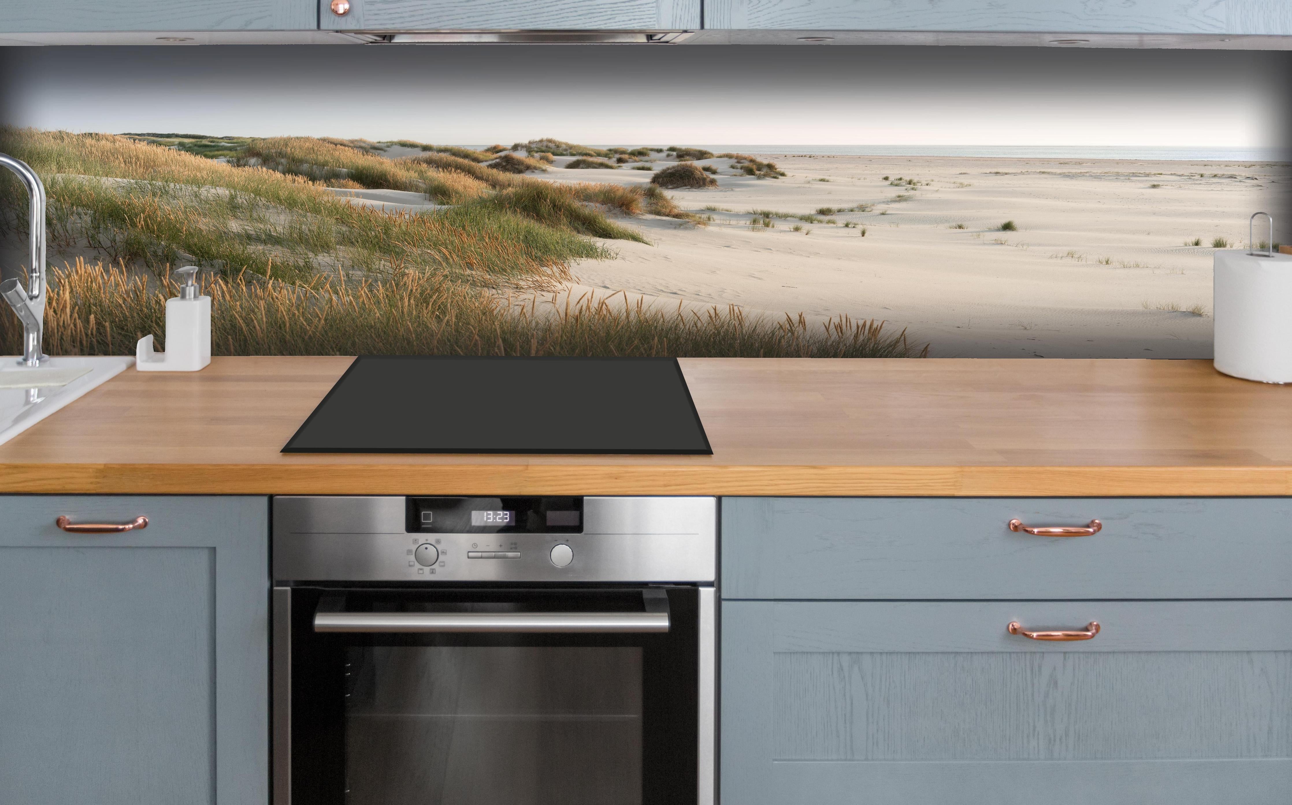 Küche - Harmonische Strandlandschaft mit sanften Sanddünen und Strandgräsern hinter weißen Hochglanz-Küchenregalen und schwarzem Wasserhahn