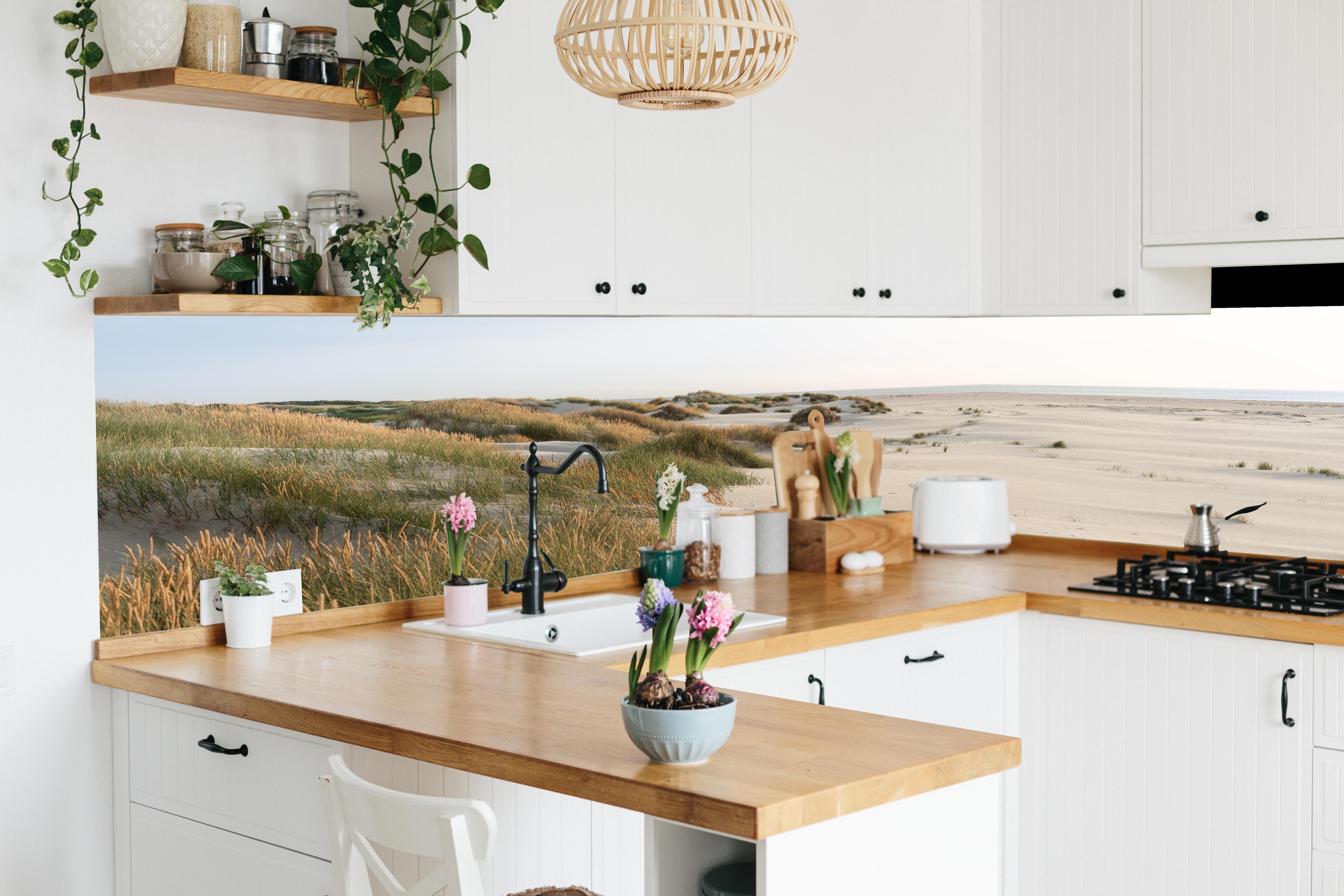 Küche - Harmonische Strandlandschaft mit sanften Sanddünen und Strandgräsern hinter weißen Hochglanz-Küchenregalen und schwarzem Wasserhahn