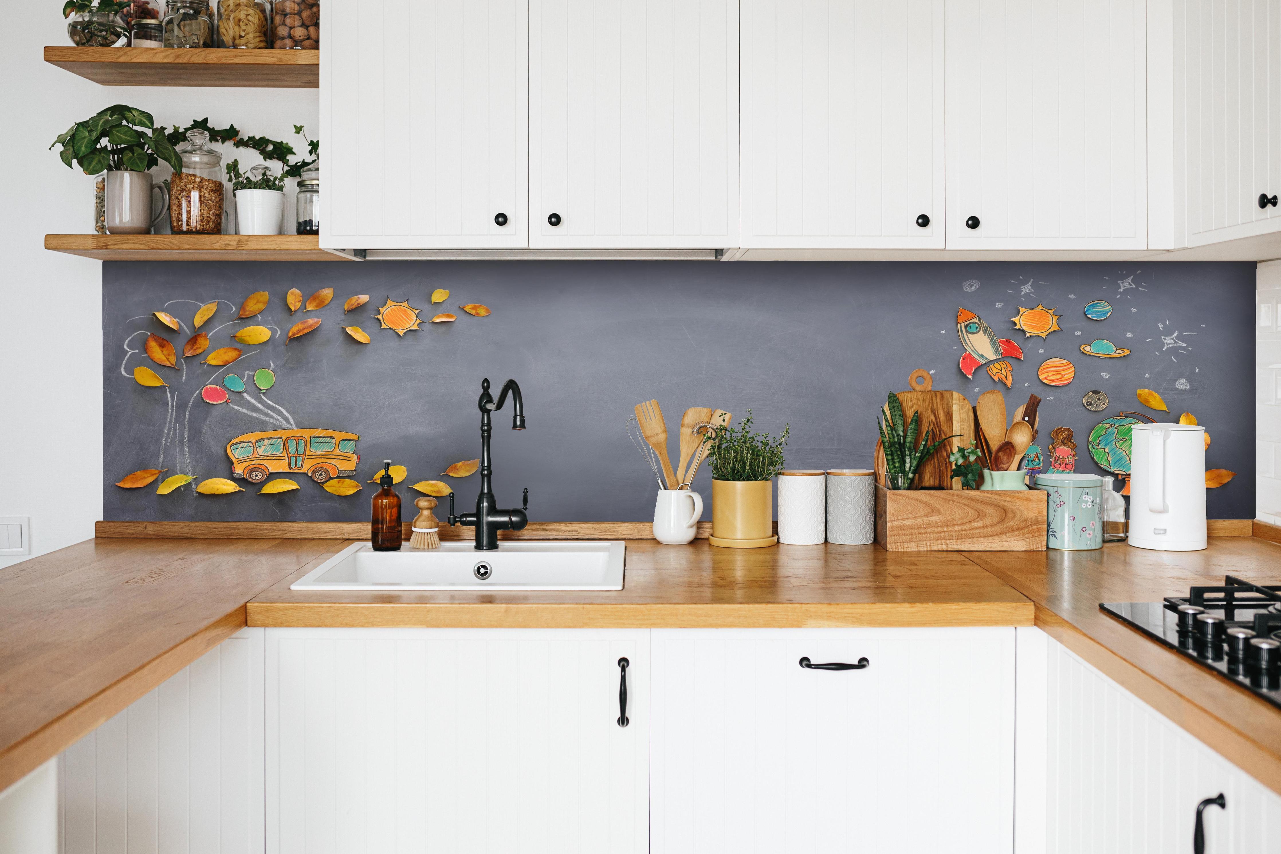 Küche - Herbstleaves und Schulbus auf Tafel hinter weißen Hochglanz-Küchenregalen und schwarzem Wasserhahn