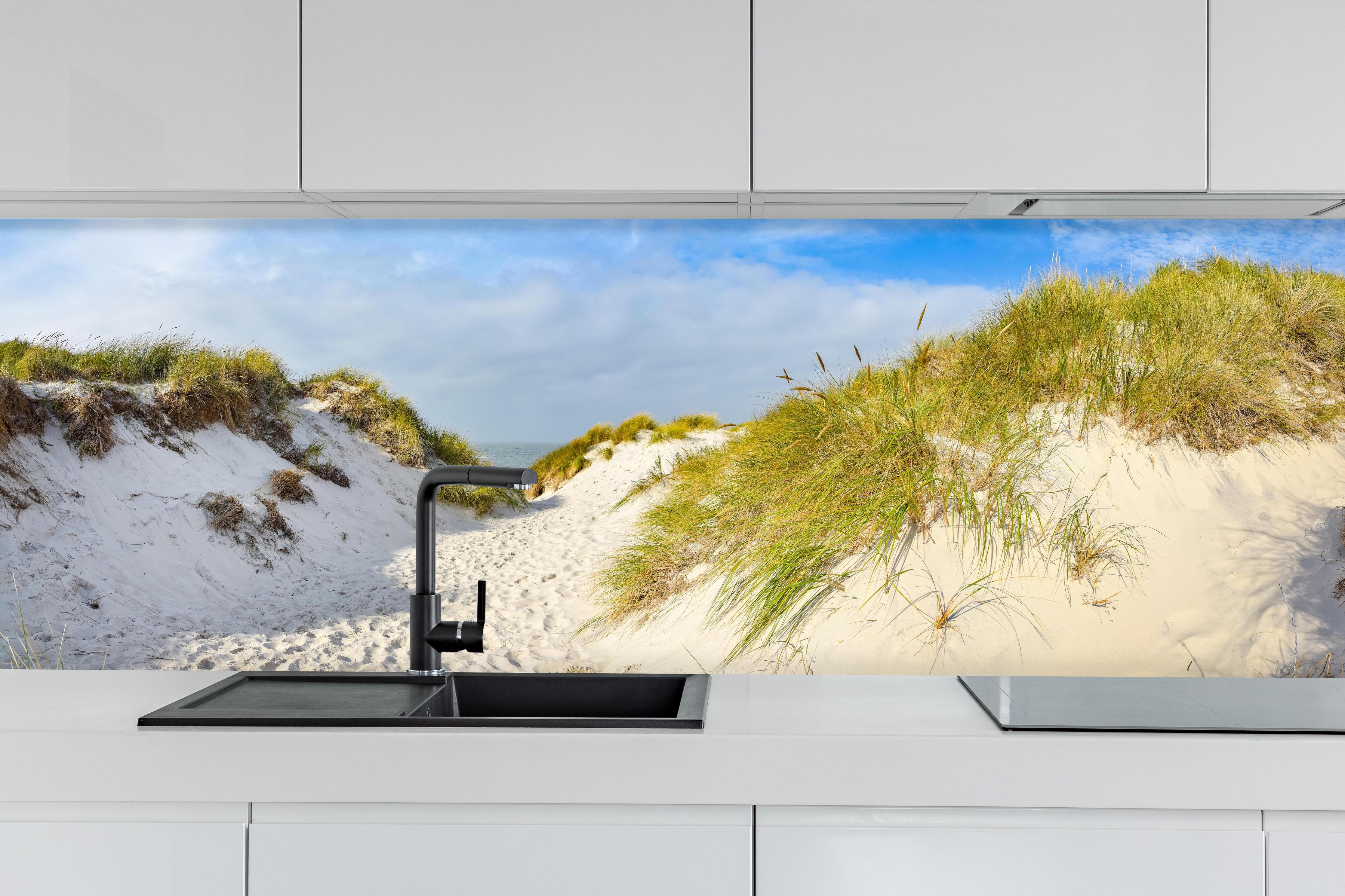 Küche - Idyllische Dünenlandschaft mit feinem Sand und grünem Gras hinter weißen Hochglanz-Küchenregalen und schwarzem Wasserhahn