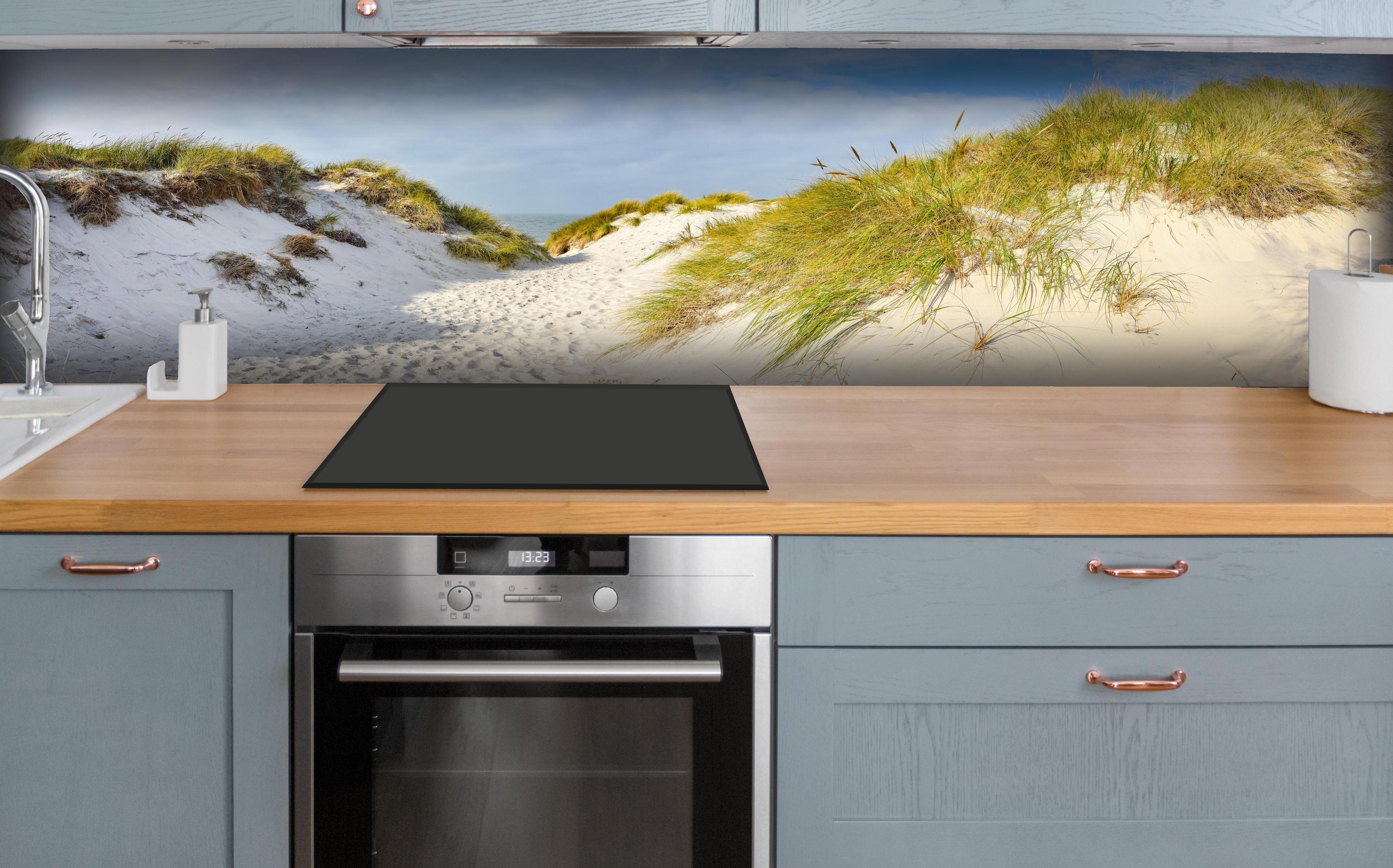 Küche - Idyllische Dünenlandschaft mit feinem Sand und grünem Gras hinter weißen Hochglanz-Küchenregalen und schwarzem Wasserhahn