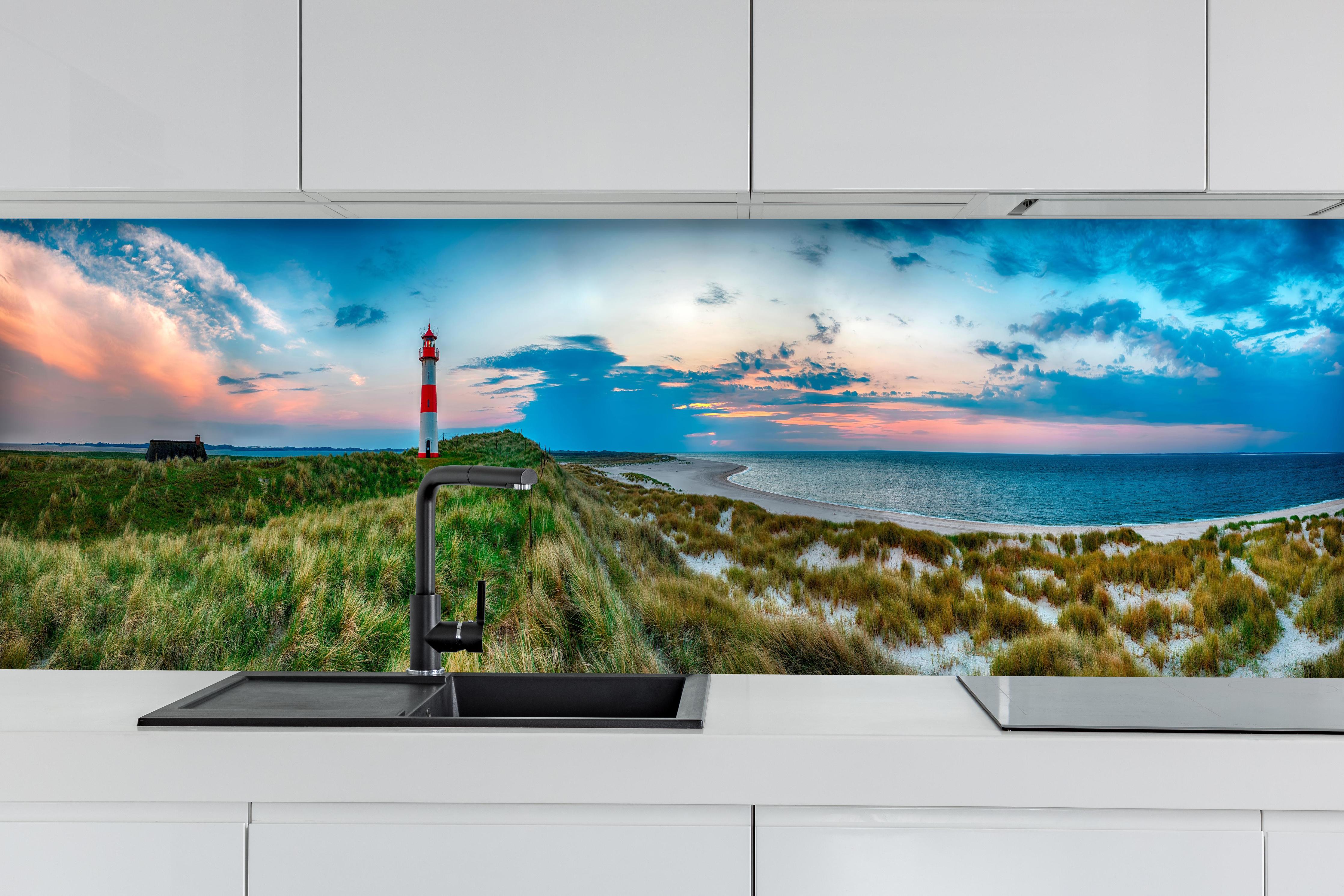 Küche - Idyllischer Leuchtturm mit traumhaften Ausblick auf den Sonnenuntergang am Meer hinter weißen Hochglanz-Küchenregalen und schwarzem Wasserhahn