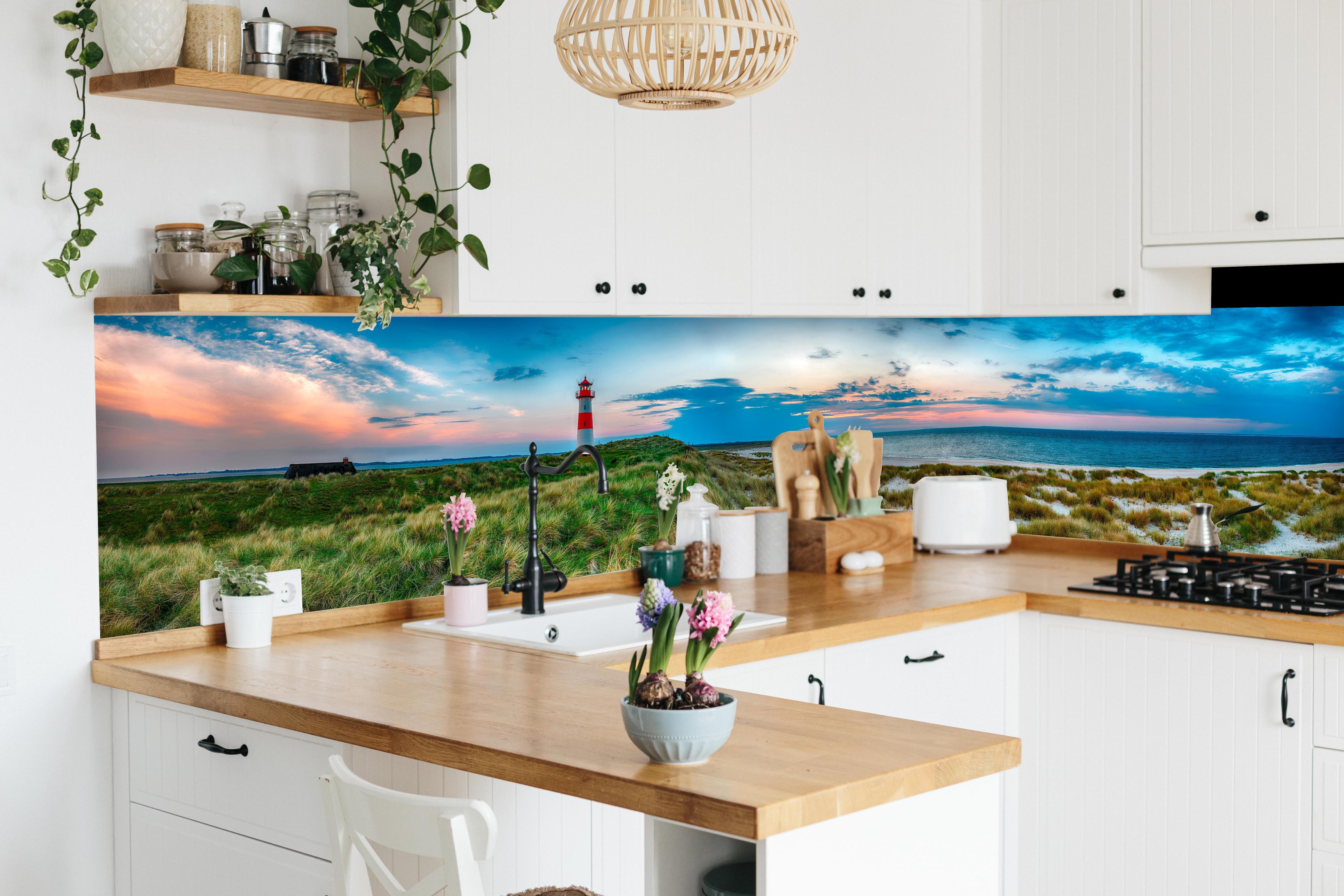 Küche - Idyllischer Leuchtturm mit traumhaften Ausblick auf den Sonnenuntergang am Meer hinter weißen Hochglanz-Küchenregalen und schwarzem Wasserhahn